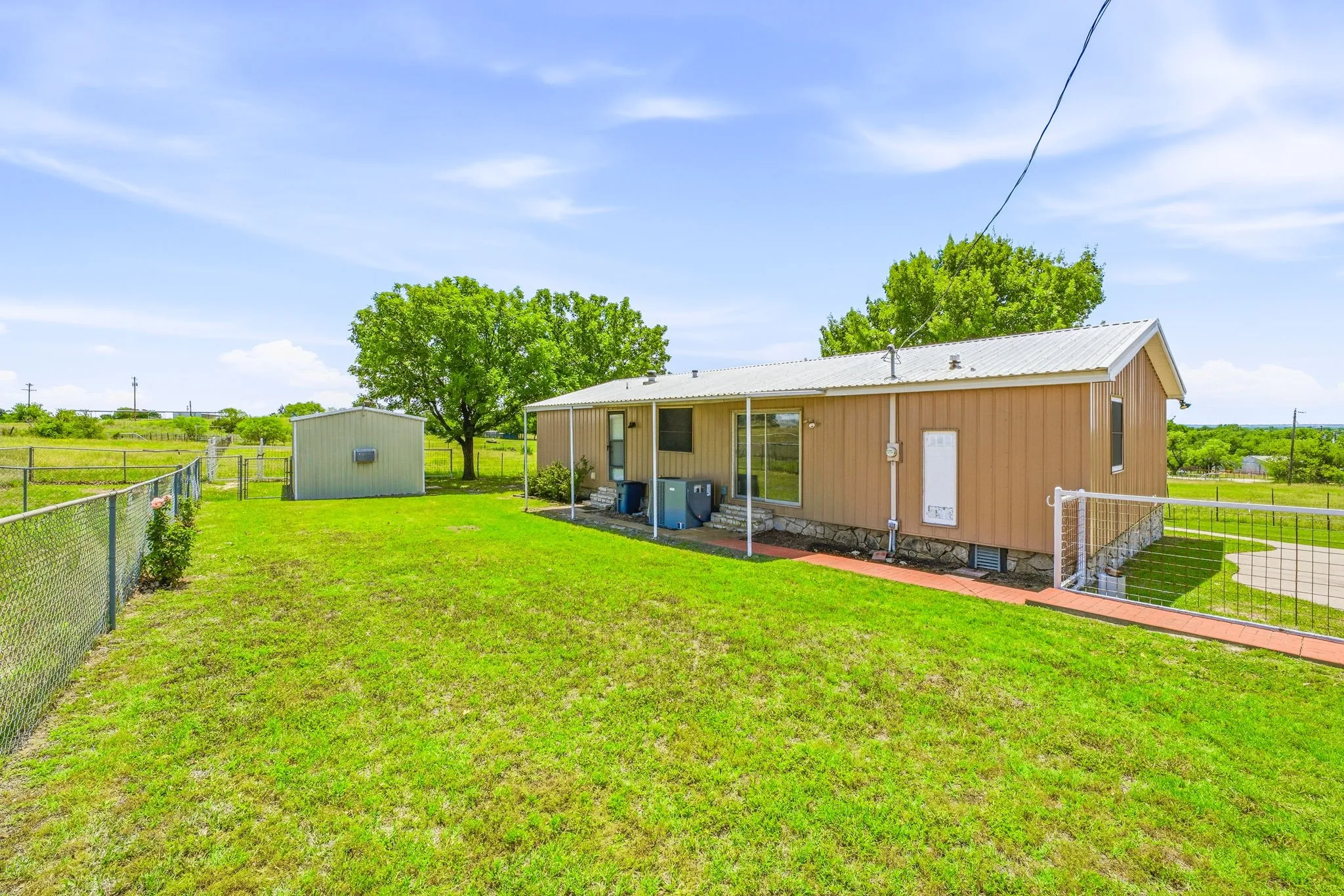 Expansive green lawn with a chain-link fence, mature trees, and a detached storage shed