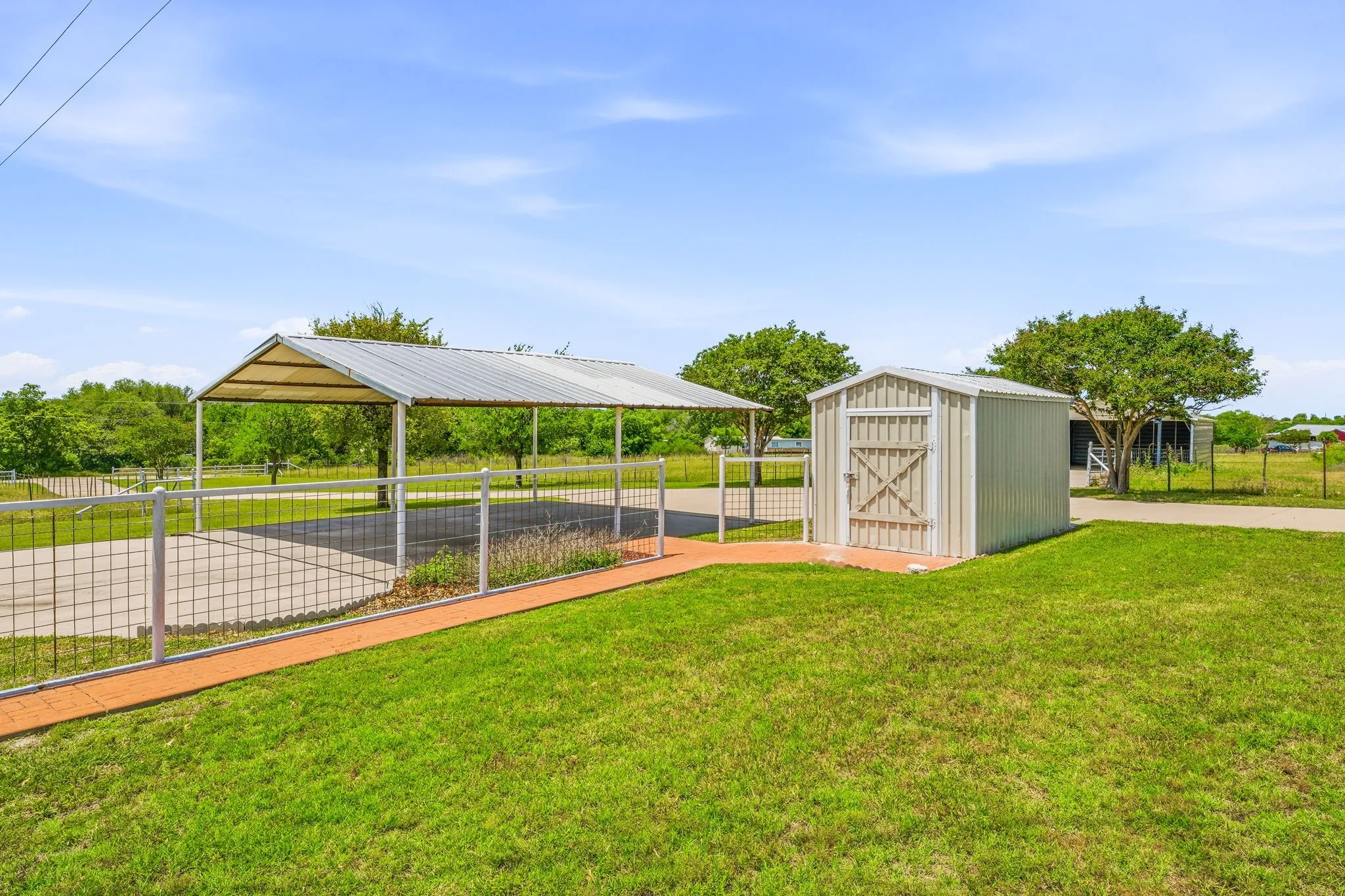 Metal carport structure with a corrugated roof, concrete pad, and white wire fencing