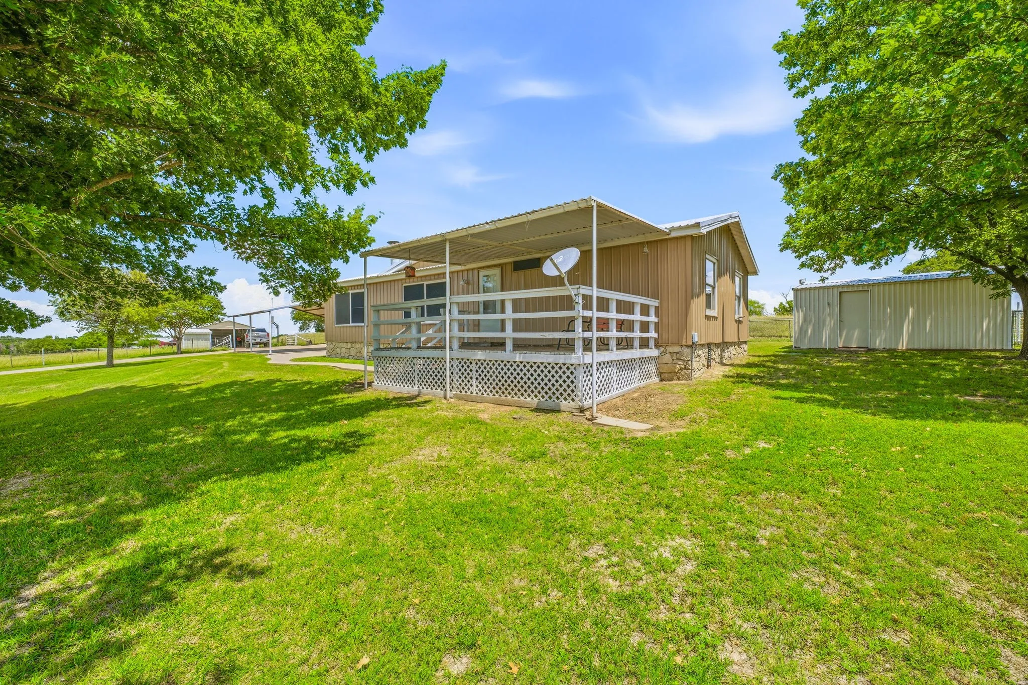 Rear exterior featuring a covered deck with white railing, brown siding, and stone foundation accents