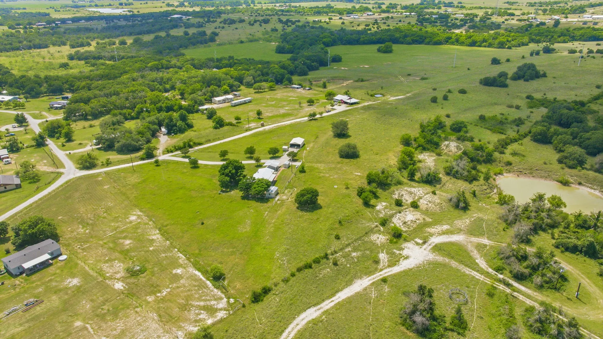 Expansive green landscape featuring varied terrain, scattered mature trees, and a visible pond