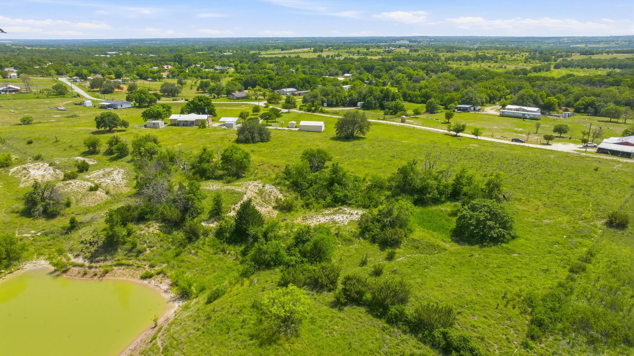 Expansive green landscape featuring varied topography, a tranquil pond, scattered trees, and distant structures