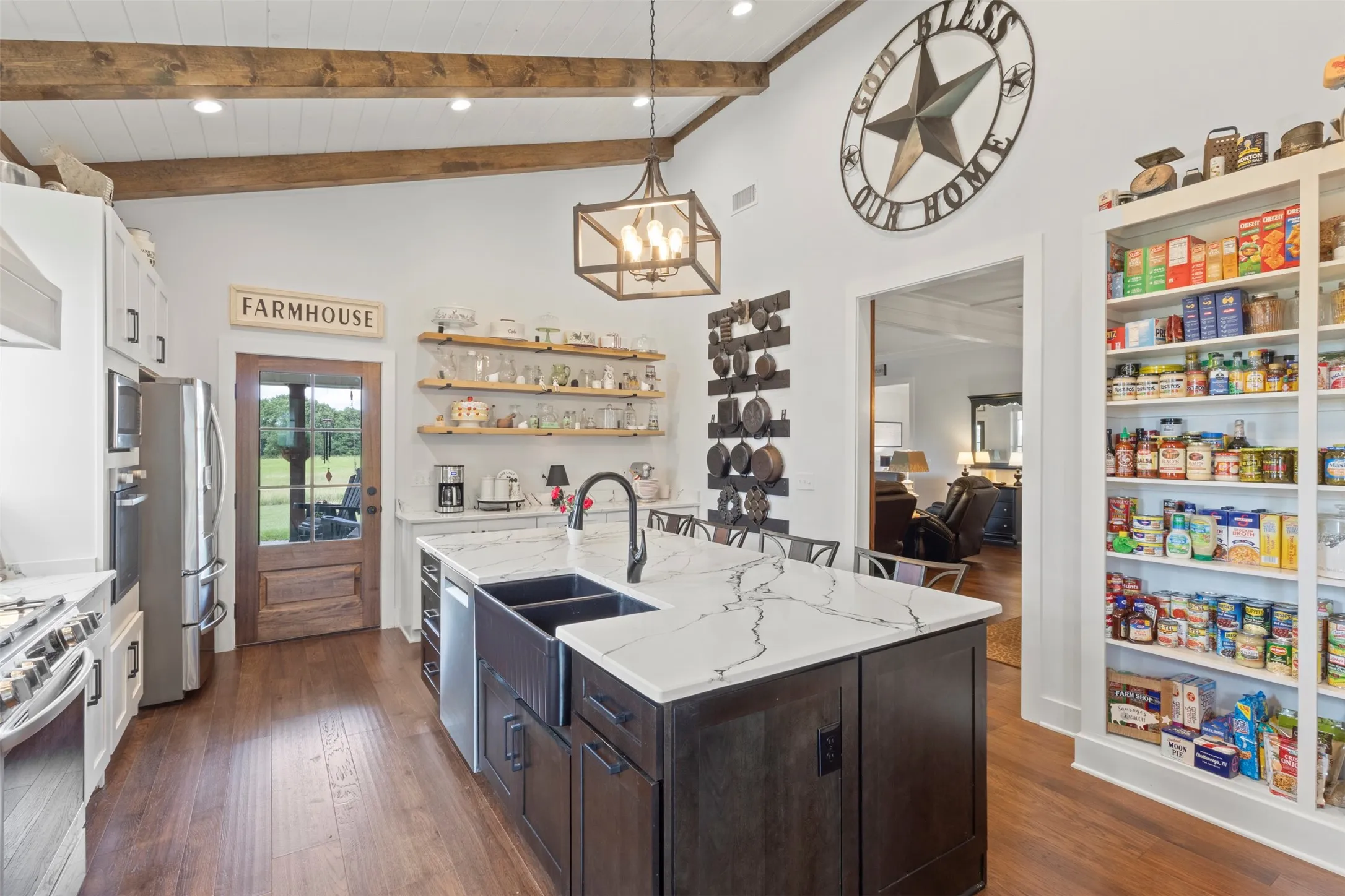 Expansive farmhouse-style kitchen featuring soaring beamed ceilings, a statement island with quartz countertops, and a gas range with convection oven—designed for both everyday cooking and effortless entertaining.
