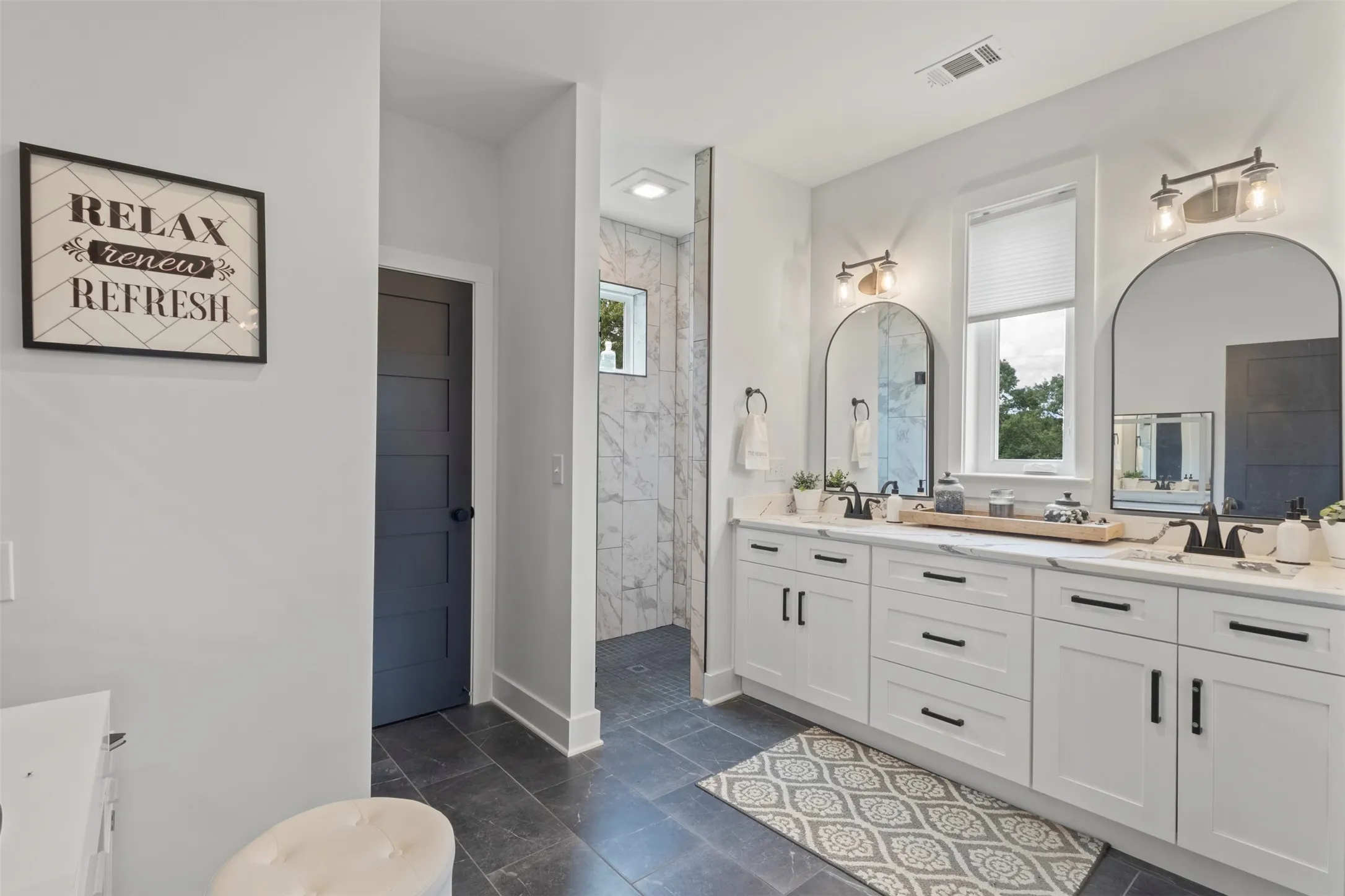 Spa-inspired primary bath featuring dual vanities, designer lighting, sleek black hardware, and a spacious walk-in shower with refined tilework—creating a polished, luxury retreat with modern country elegance.