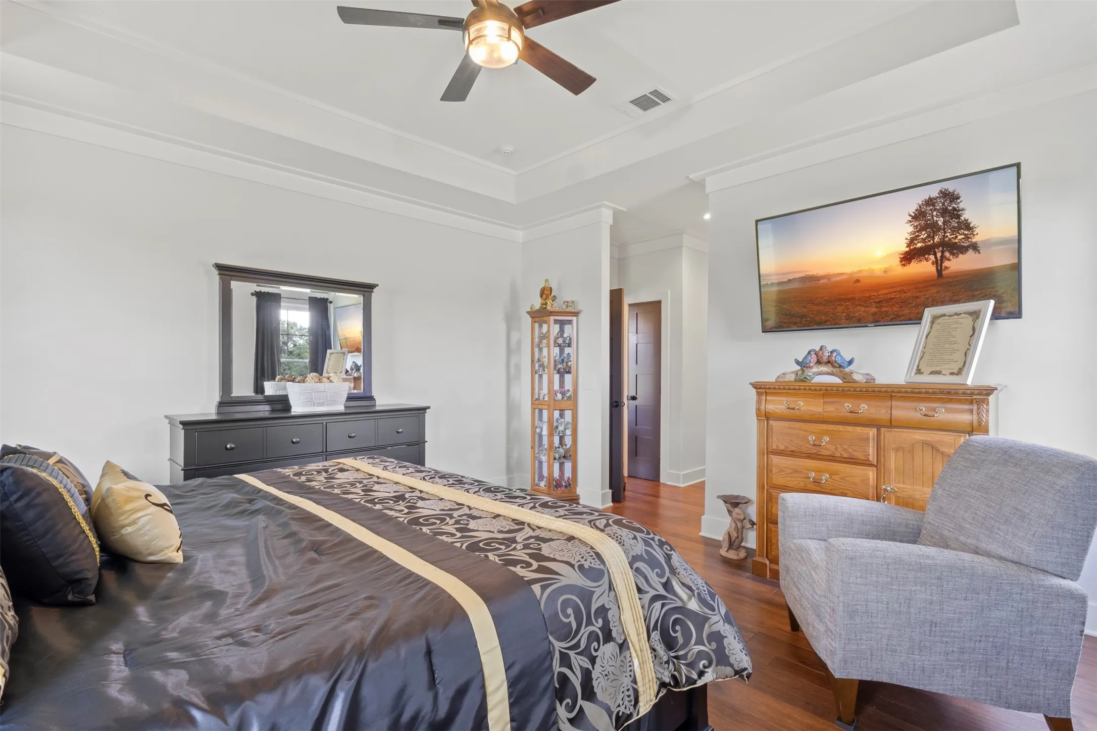 Elegant bedroom retreat featuring rich hardwood flooring, tray ceiling detail, elevated trim work, and serene acreage views—offering a refined blend of comfort, privacy, and timeless country luxury.