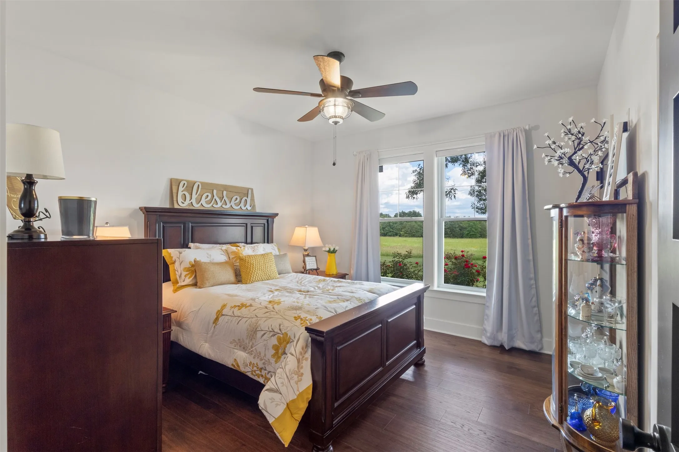 Comfortable second bedroom featuring warm hardwood flooring, abundant natural light, and peaceful acreage views—offering an inviting retreat with classic country elegance and refined simplicity.