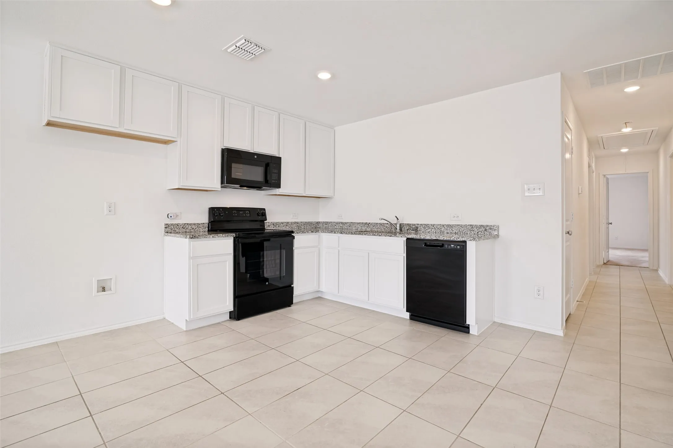 Modern kitchen area featuring white cabinetry, granite-finish countertops, and tile flooring