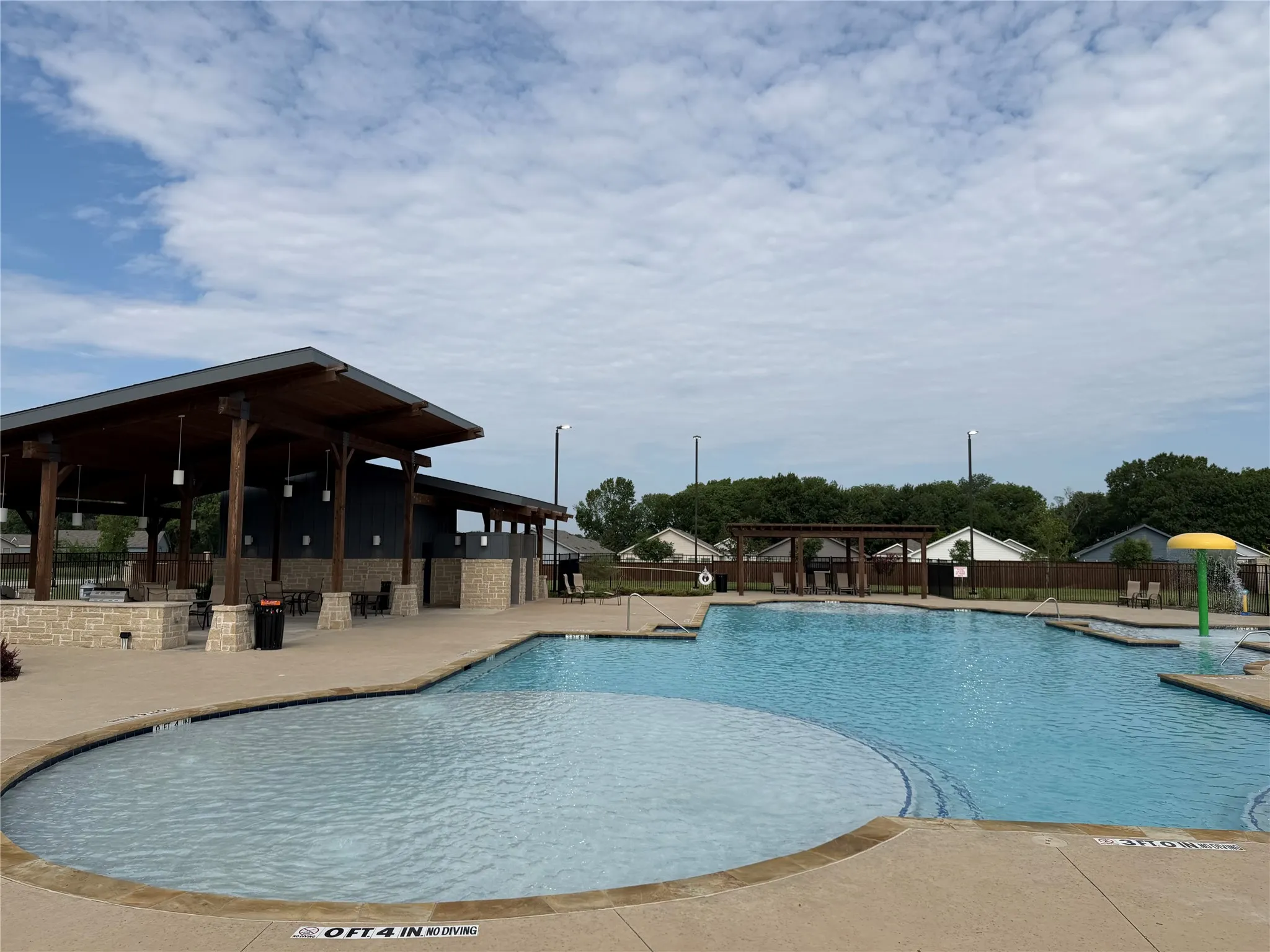 Expansive community pool area featuring a multi-depth swimming pool, integrated shallow wading area, and a shaded pavilion with stone columns
