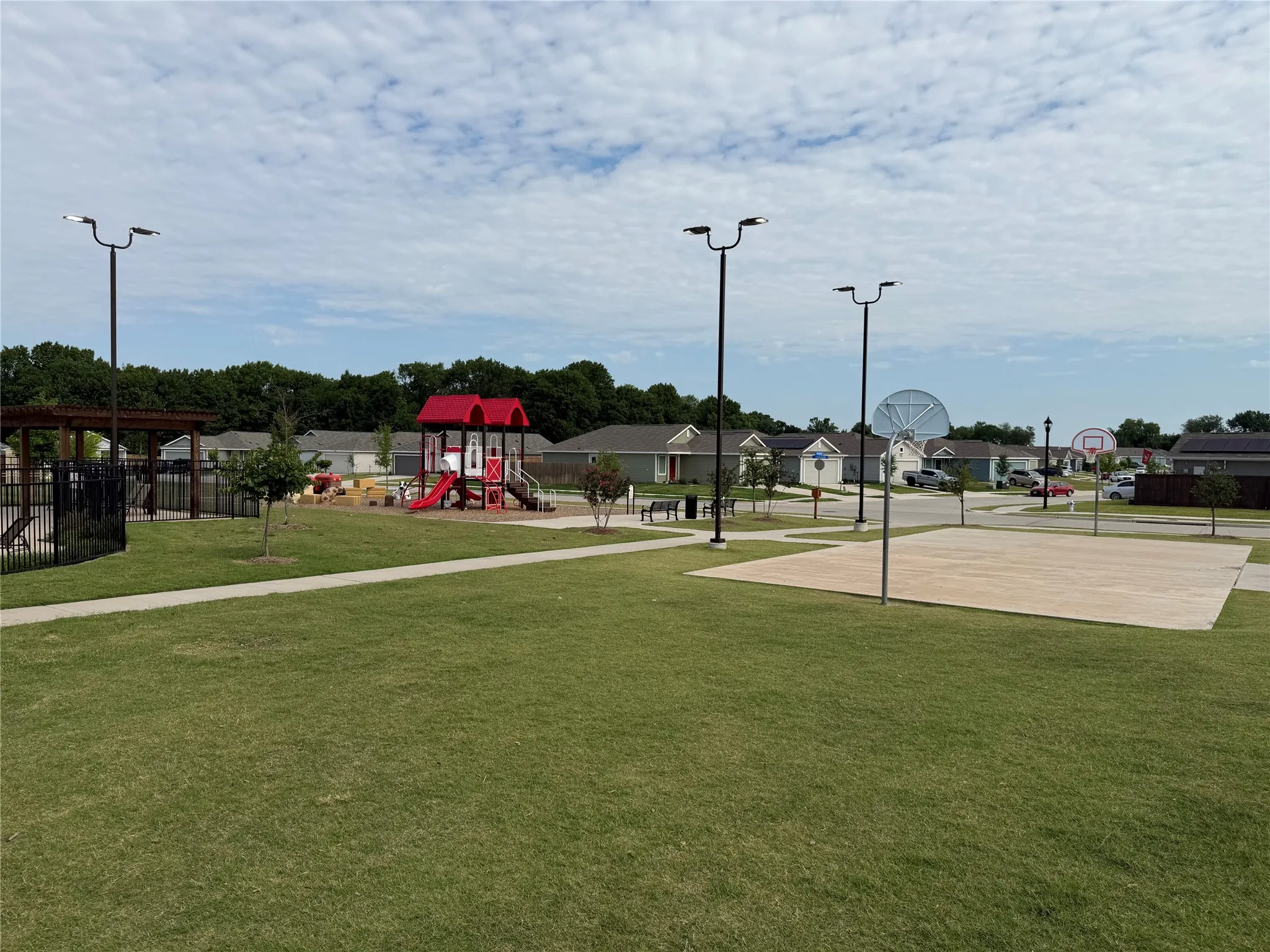 Community recreation area featuring a playground with red and white slides, a multi-sport court, and green spaces