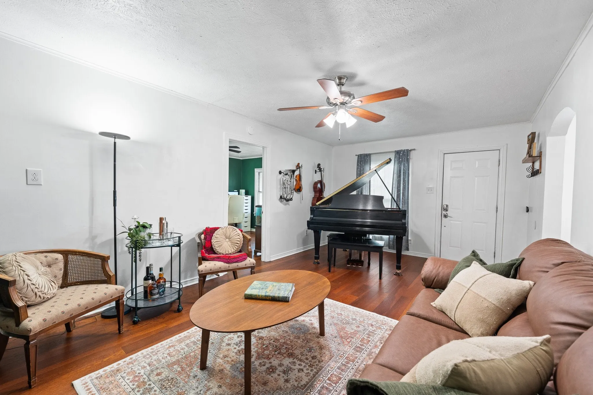 Living area featuring wood-finish flooring, a ceiling fan with integrated lighting, a white paneled entry door, and an arched doorway