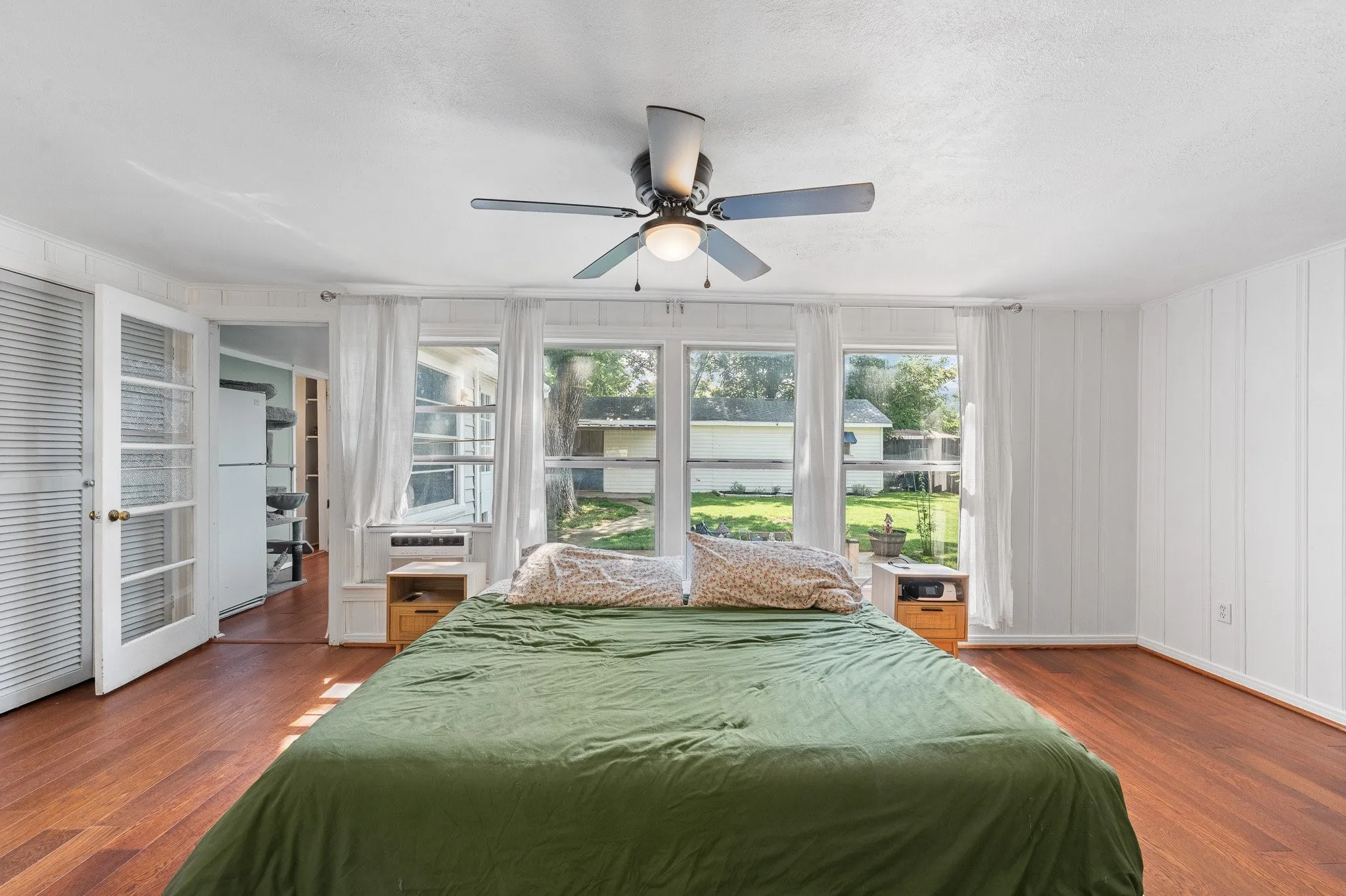 Bedroom featuring wood-finish flooring, a ceiling fan with light fixture, and multiple windows providing natural light