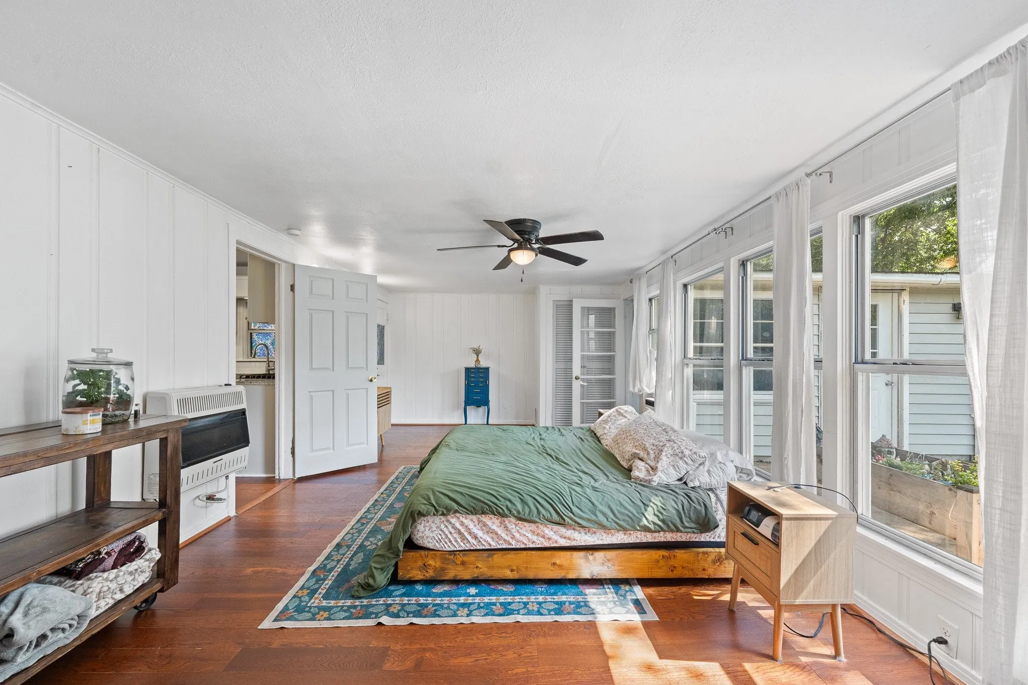 Bright room featuring extensive natural light, wood-finish flooring, white paneling, a ceiling fan, and multiple windows