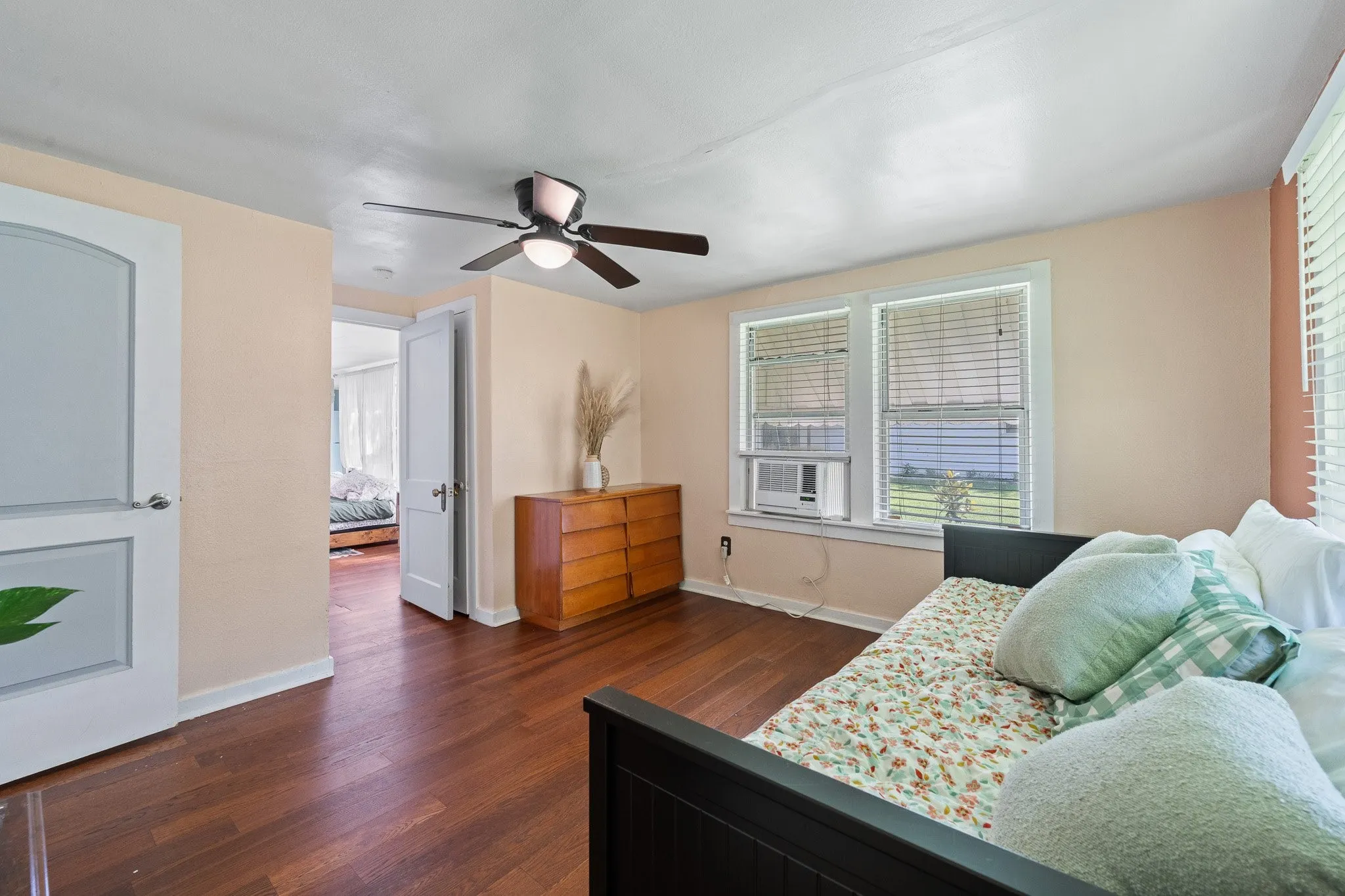 Wood-finish flooring throughout, featuring a ceiling fan with integrated lighting, multiple windows with blinds, and painted interior walls