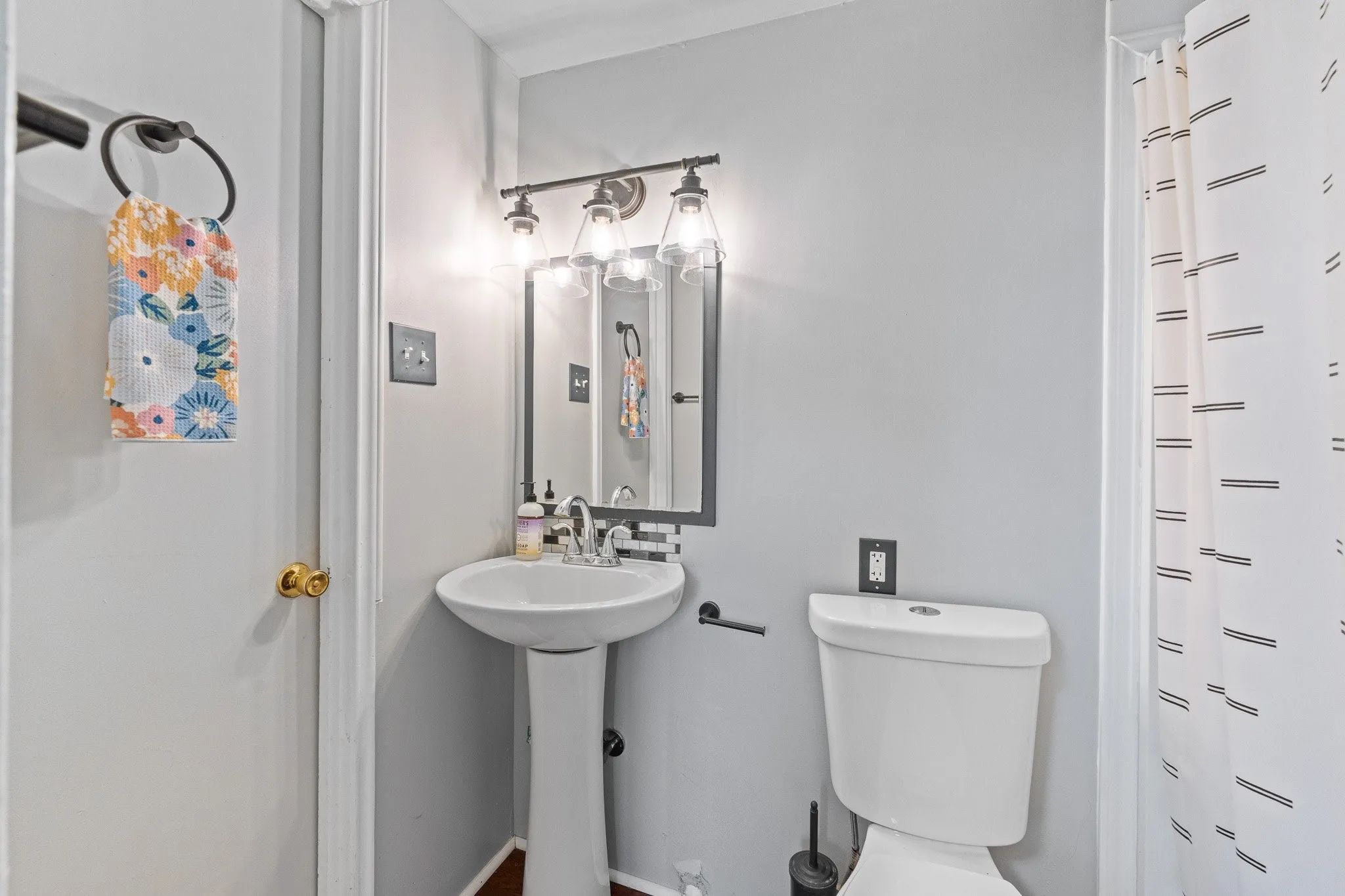 Pedestal sink with coordinating mirror and light fixture, featuring a white toilet and shower area