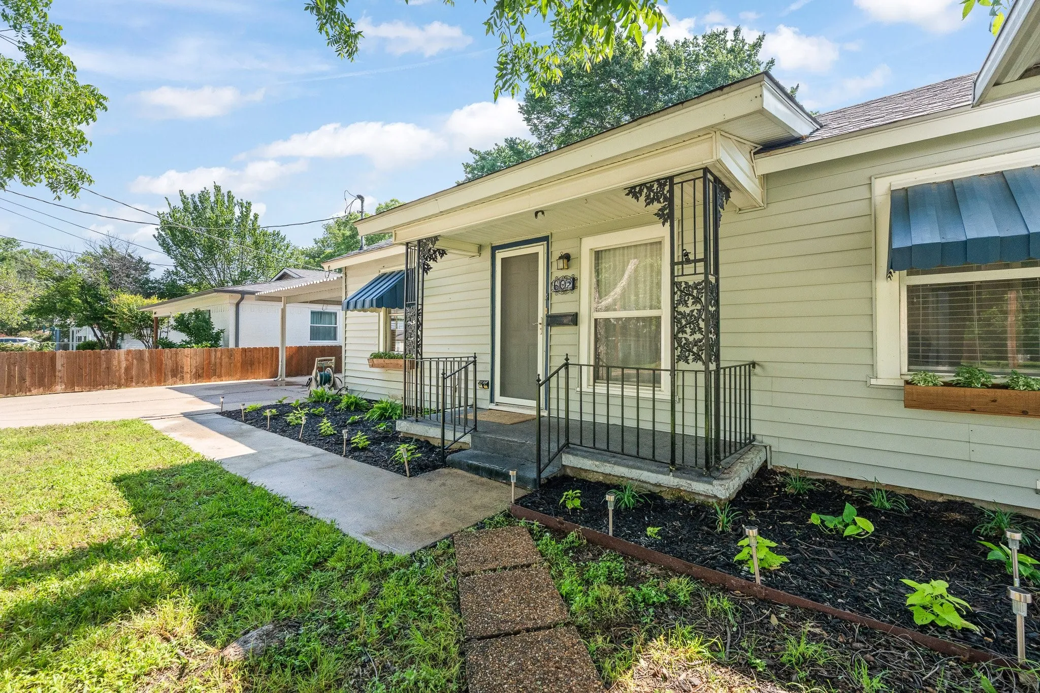 Light-colored horizontal siding exterior featuring a covered porch entry with ornate black metal supports and railings