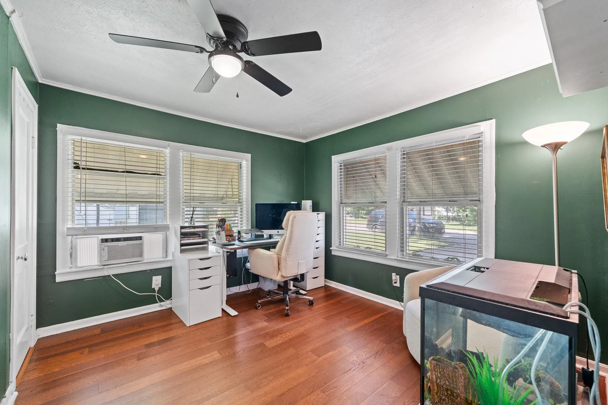 Room featuring wood-finish flooring, two large windows with blinds, and painted green walls