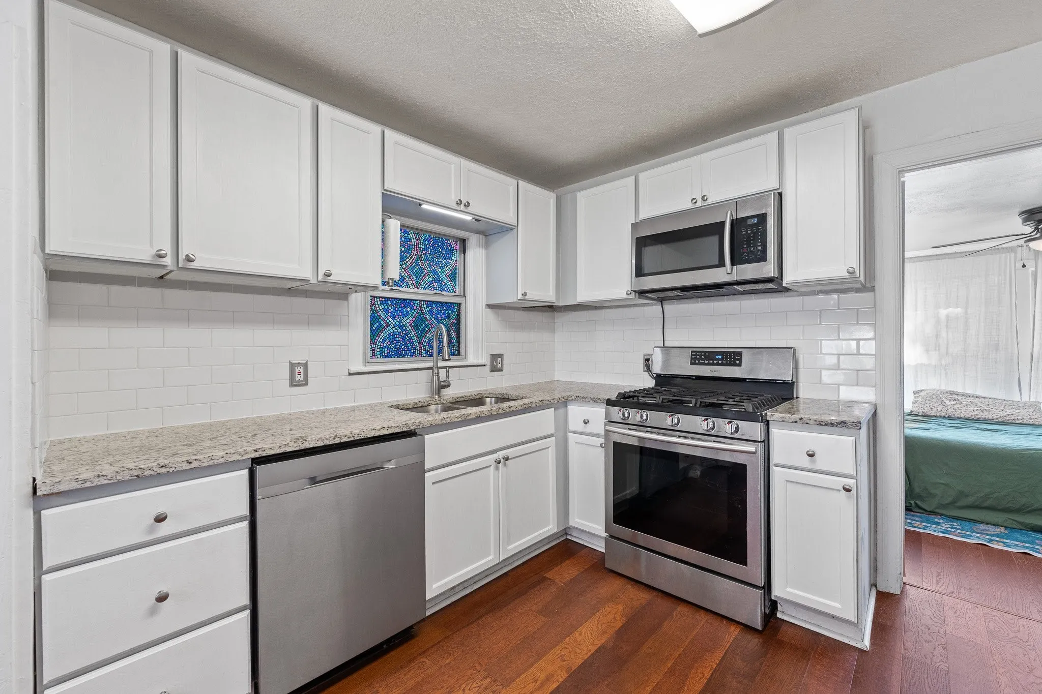 Kitchen featuring white cabinetry, granite countertops, stainless steel appliances, a subway tile backsplash, and wood-finish flooring