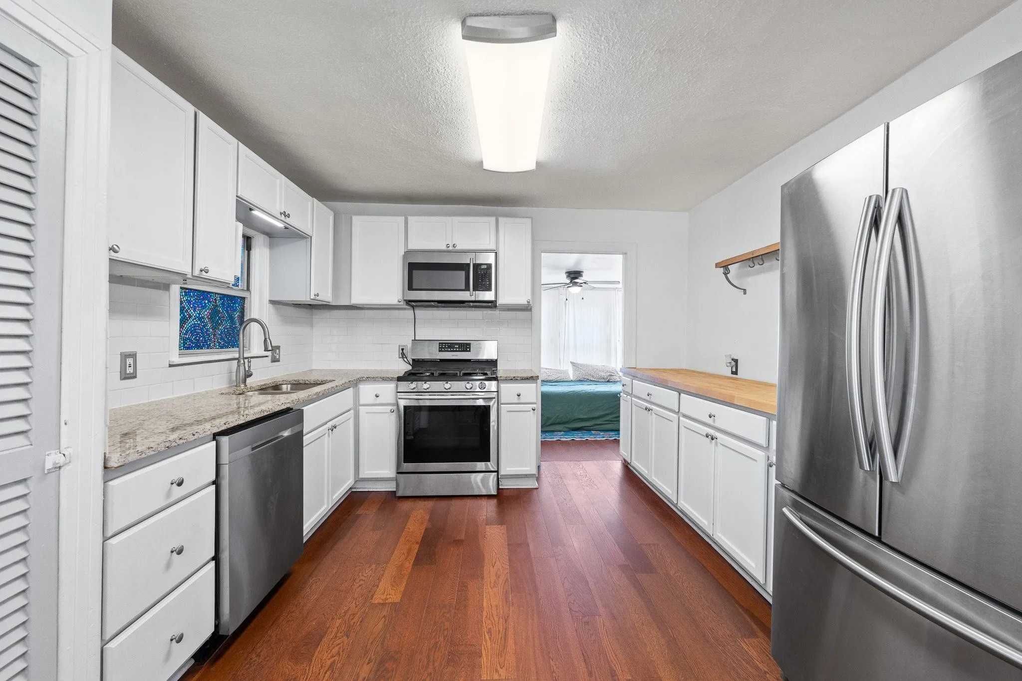 Kitchen featuring wood-finish flooring, white cabinetry with silver hardware, and stainless steel appliances