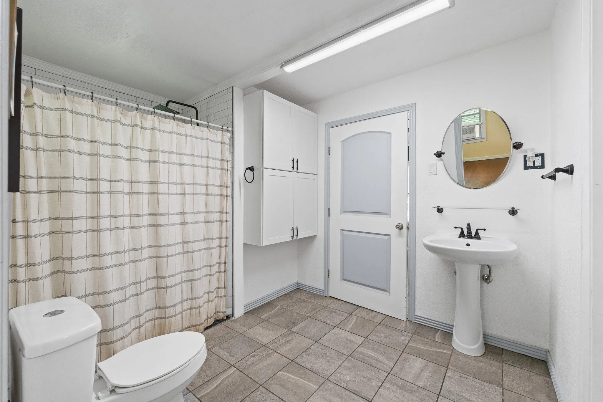 Bathroom featuring a tiled shower enclosure, white pedestal sink, and gray-toned floor tiling
