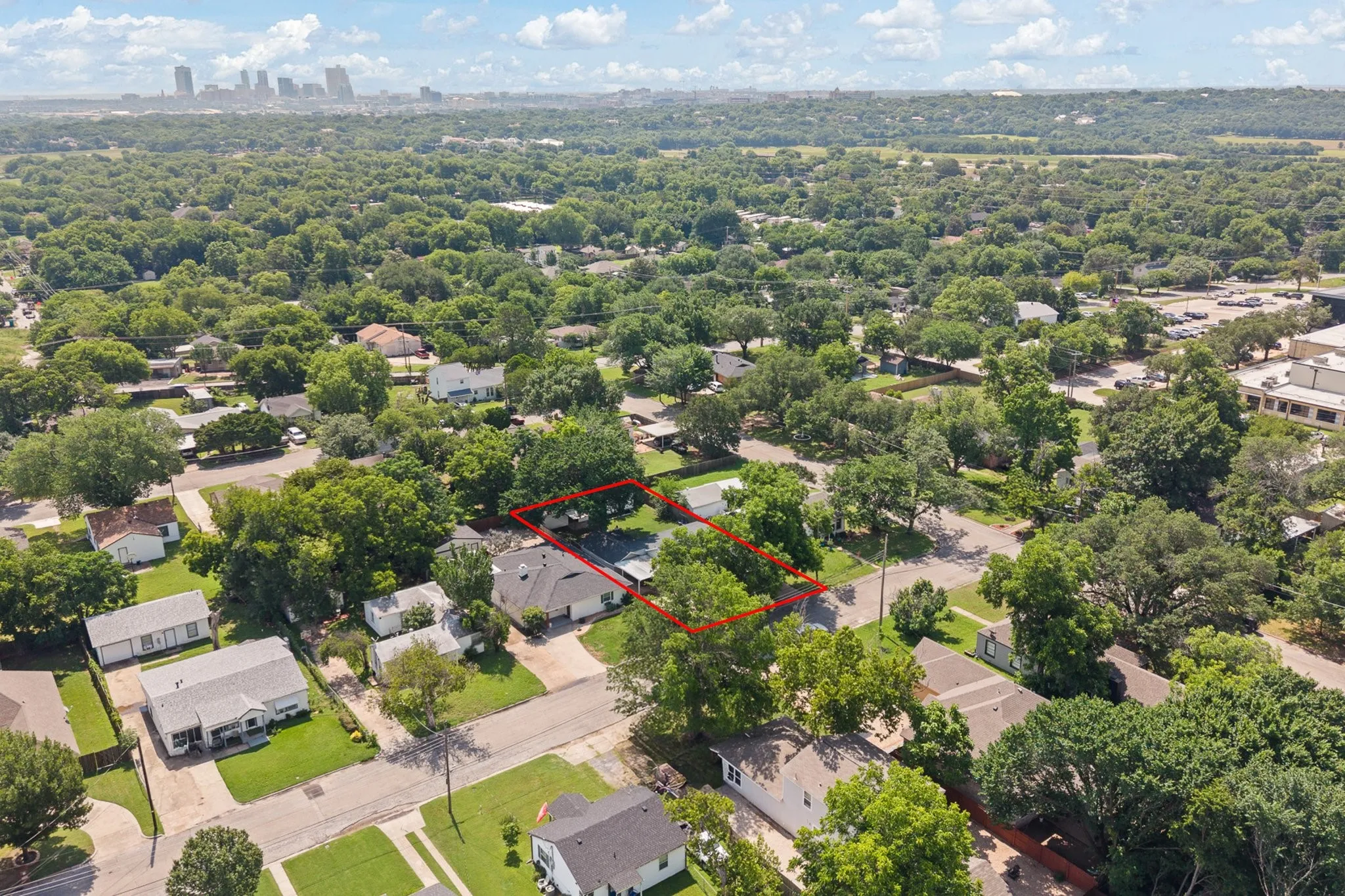Aerial perspective showcasing a residential property with a dark shingle roof, surrounded by mature trees