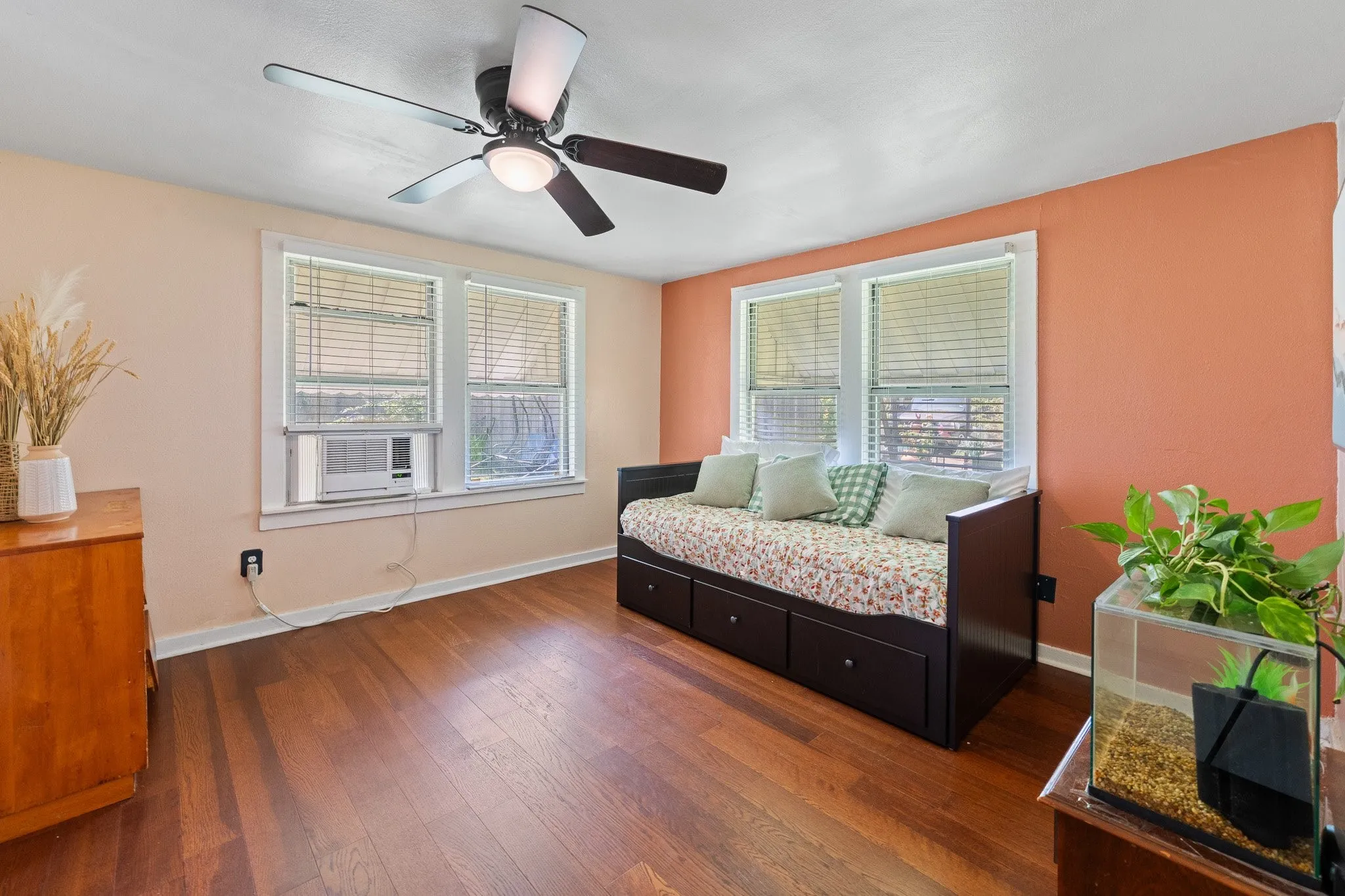 Warm-toned room featuring wood-finish flooring, two windows with blinds, a ceiling fan with integrated lighting, and painted walls