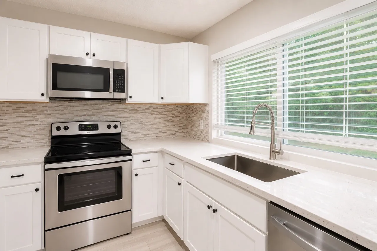 Modern kitchen featuring white shaker cabinetry, stainless steel appliances, light-toned countertops, and a mosaic tile backsplash