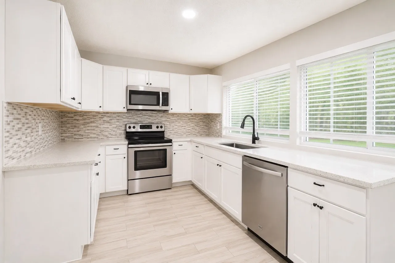 Kitchen featuring white cabinetry with black hardware, stainless steel appliances, light-colored countertops, a mosaic tile backsplash, and light wood-finish flooring