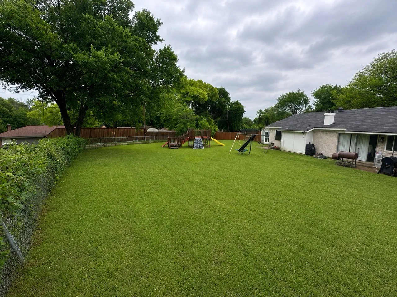 Expansive green lawn with mature perimeter trees and a wood privacy fence
