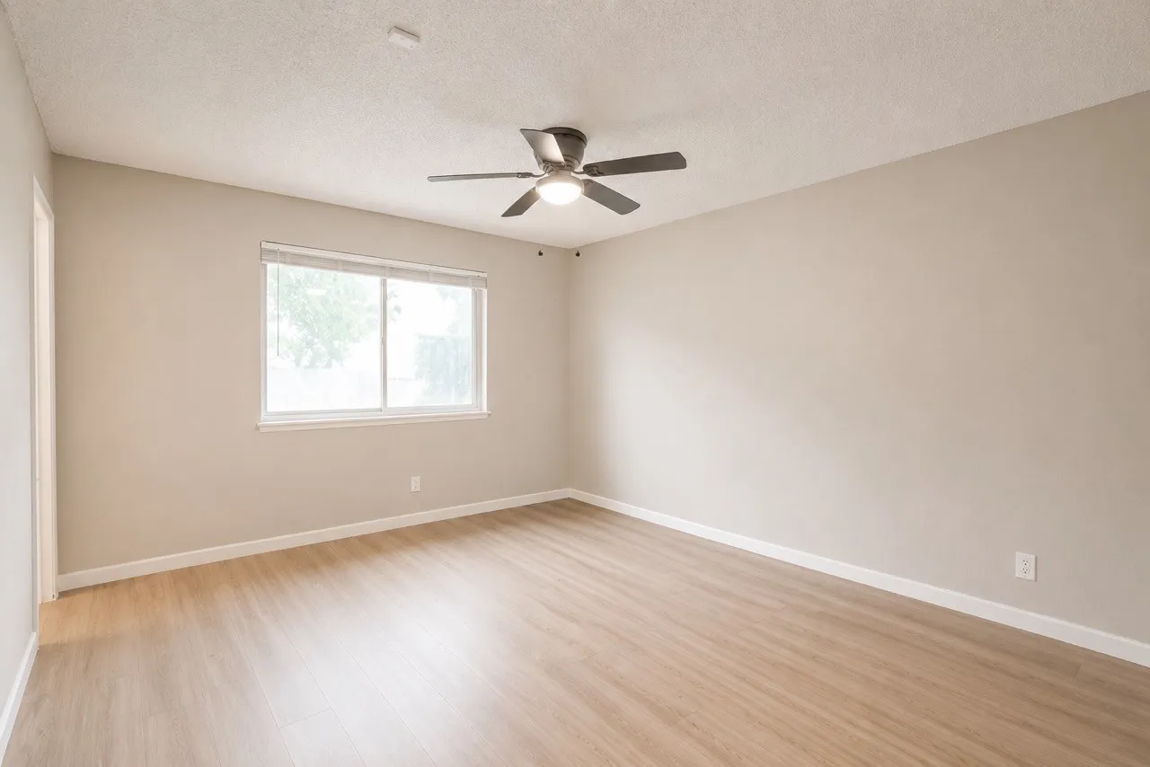Spacious room featuring light wood-finish flooring, neutral wall tones, and a ceiling fan with integrated lighting