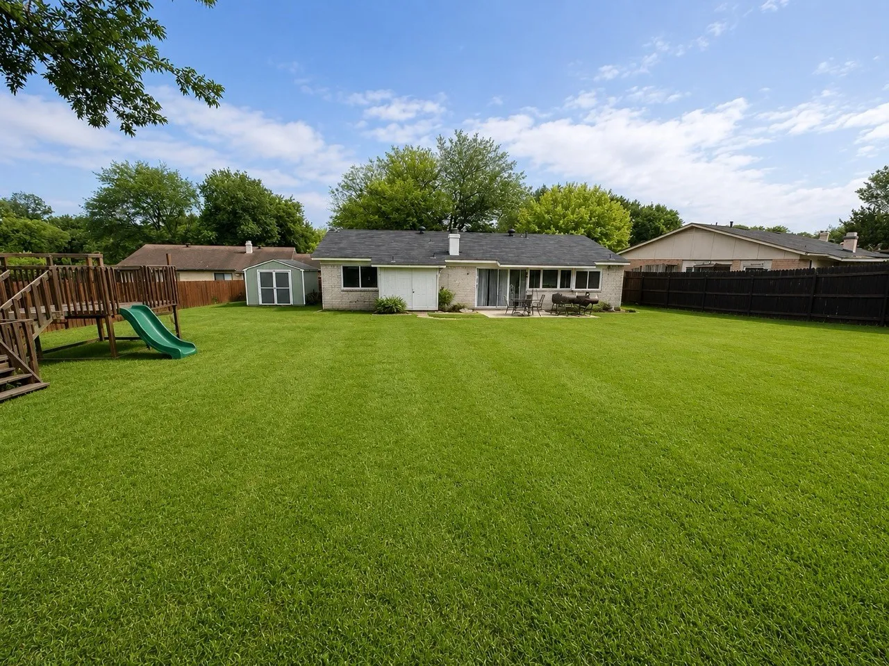 Expansive backyard featuring a lush lawn, a detached storage shed, and a stone patio area