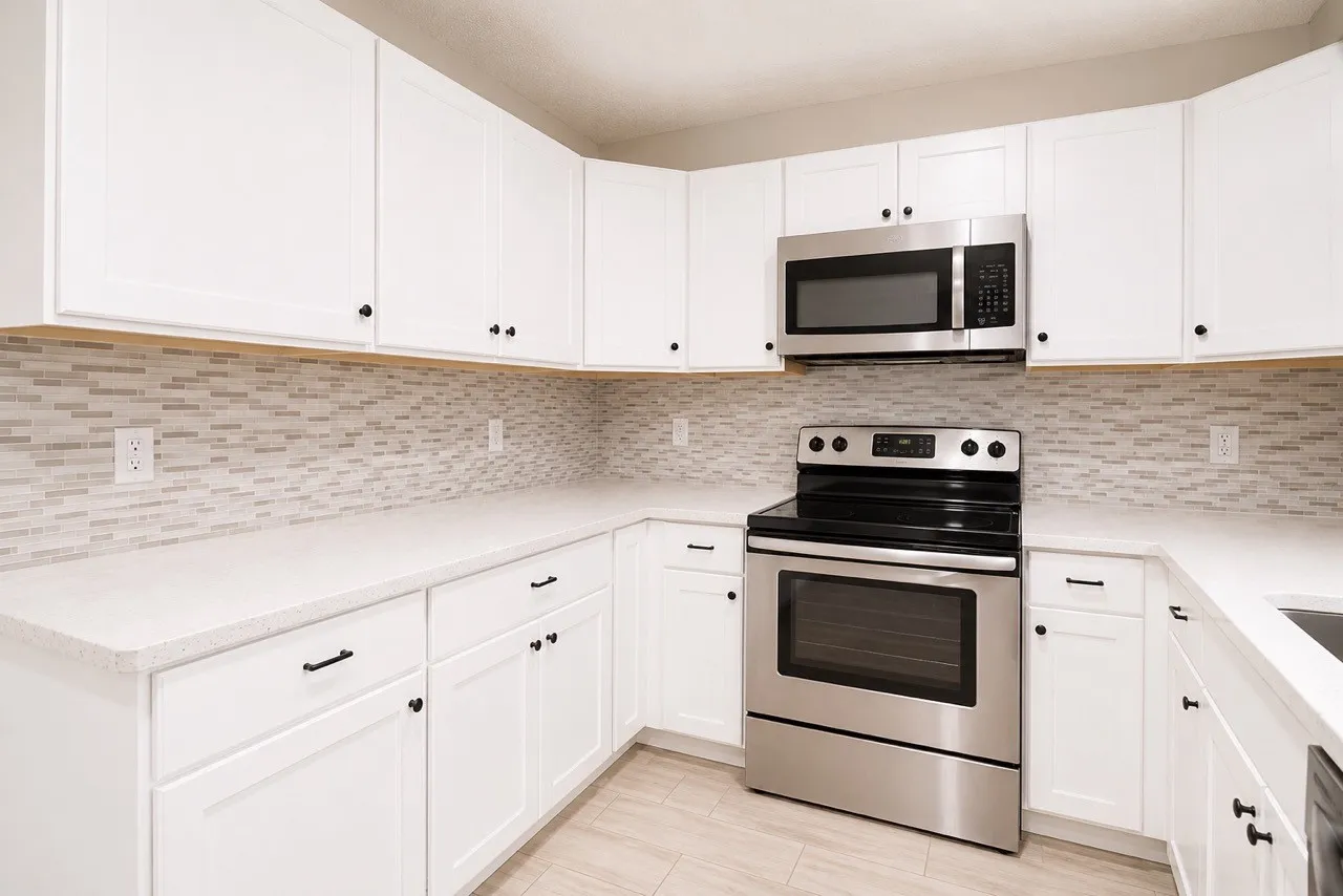 Kitchen featuring white cabinetry with black hardware, light-colored countertops, a mosaic tile backsplash, stainless steel range, and an over-the-range microwave