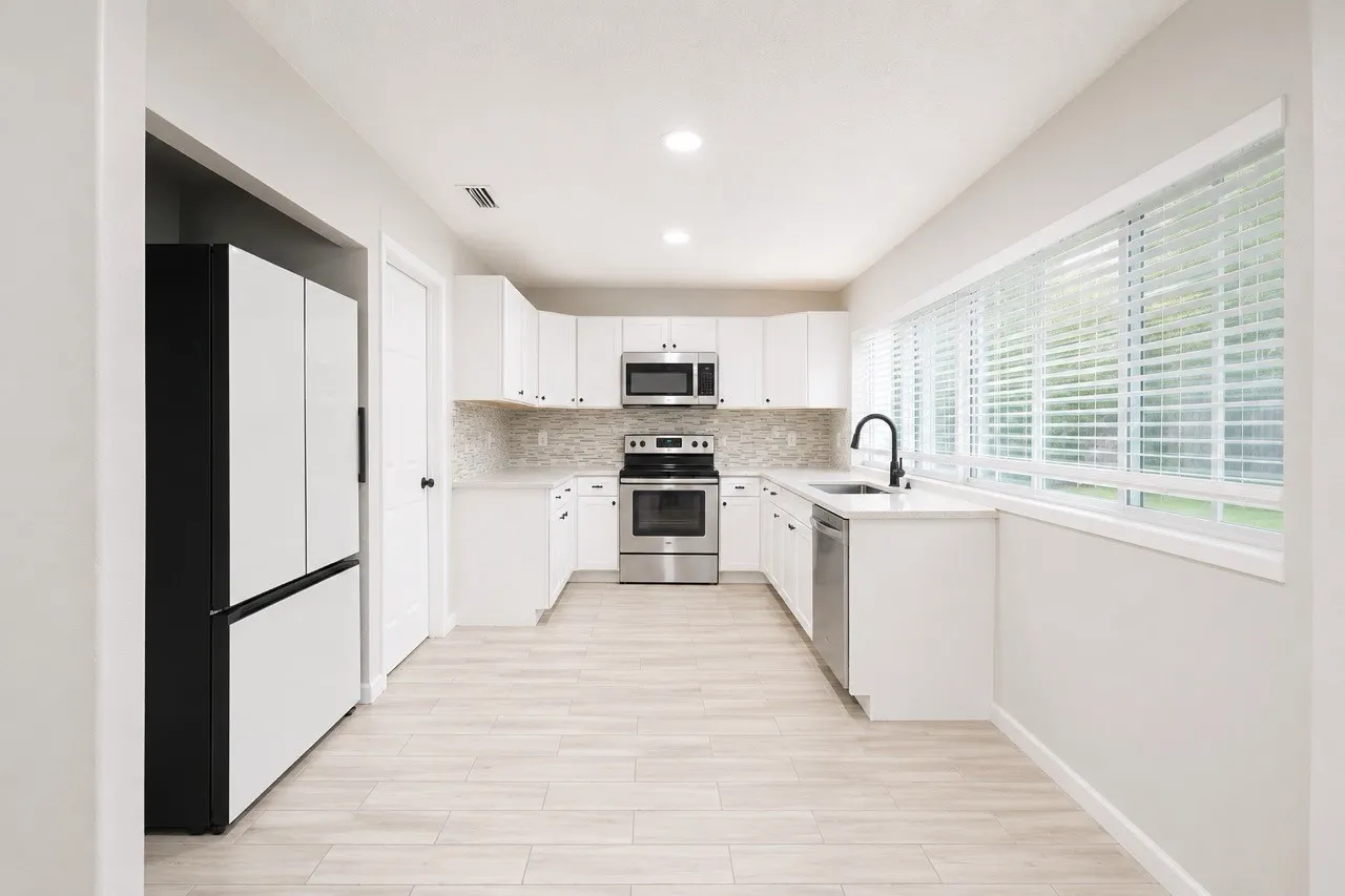 Bright kitchen featuring white cabinetry, stainless steel appliances, a tile backsplash, and wood-finish flooring