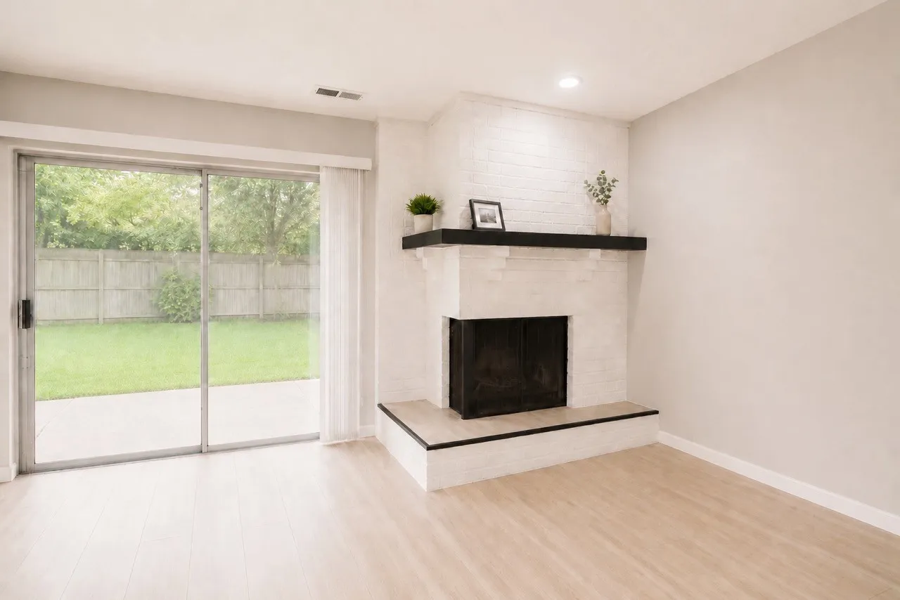 Living area featuring light wood-finish flooring, a white brick fireplace with a dark mantel, and sliding glass doors opening to a private patio and fenced backyard