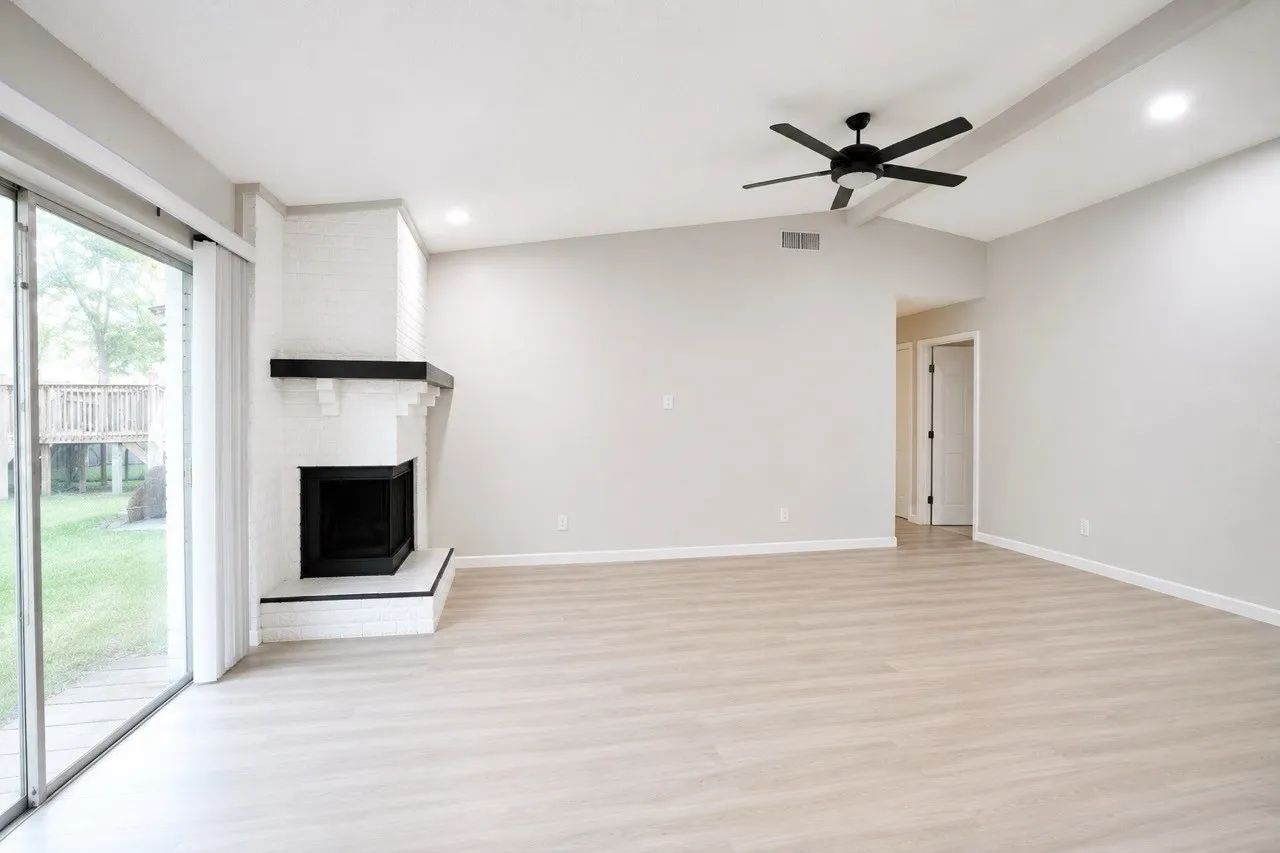 Spacious living area featuring a corner fireplace with a black mantel, wood-finish flooring, and a contemporary ceiling fan