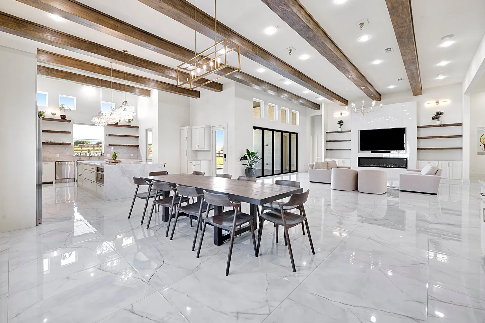 Spacious open-concept interior featuring light-toned large format flooring, exposed wood-finish ceiling beams, and a contemporary linear chandelier