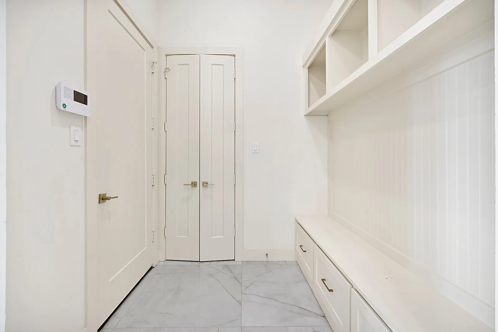 Entryway featuring built-in shelving with storage cubbies and beadboard backing, a built-in bench with drawers, white paneled doors, and large format tile flooring