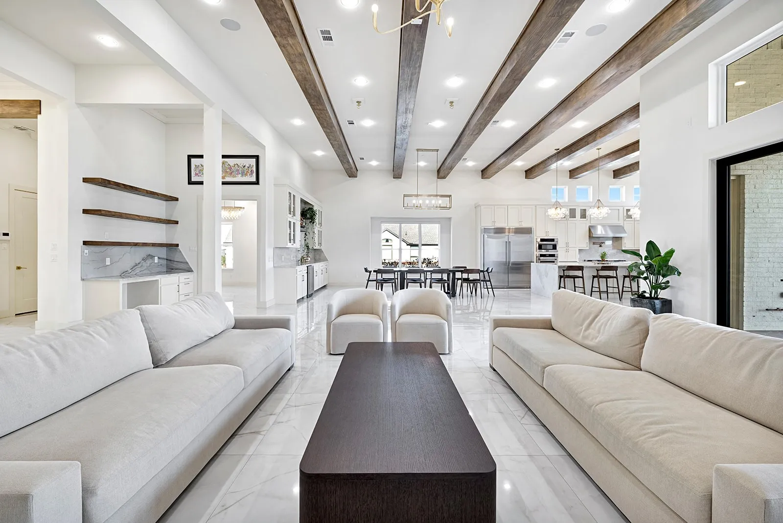 Spacious open-concept interior featuring vaulted ceilings with exposed wood beams, bright white walls, and large format tile flooring