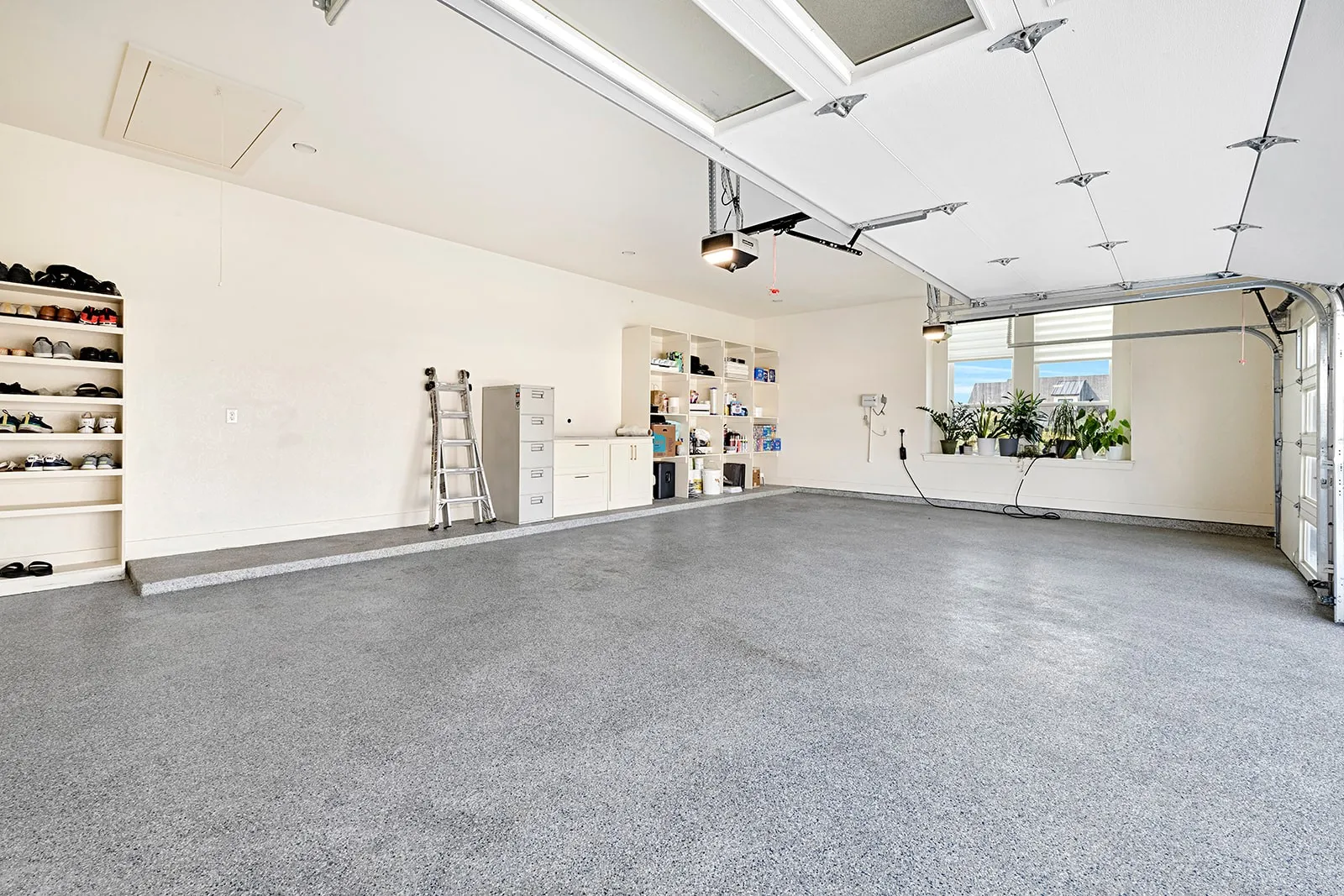 Spacious garage featuring a durable epoxy-coated concrete floor, built-in shelving, ample natural light from a large window, and automatic garage door openers