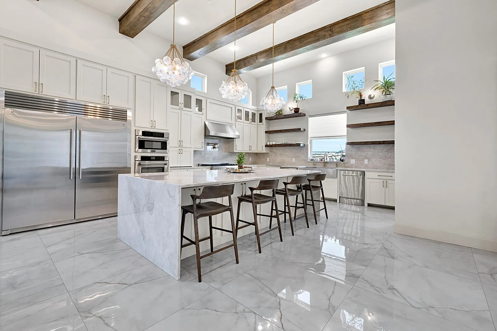 Gourmet kitchen featuring a large waterfall island, stainless steel appliances, white cabinetry, and decorative wood-finish ceiling beams