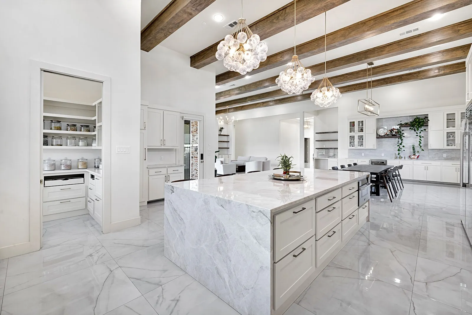 Spacious kitchen featuring a large waterfall island with integrated cabinetry, wood-finish ceiling beams, and polished tile flooring