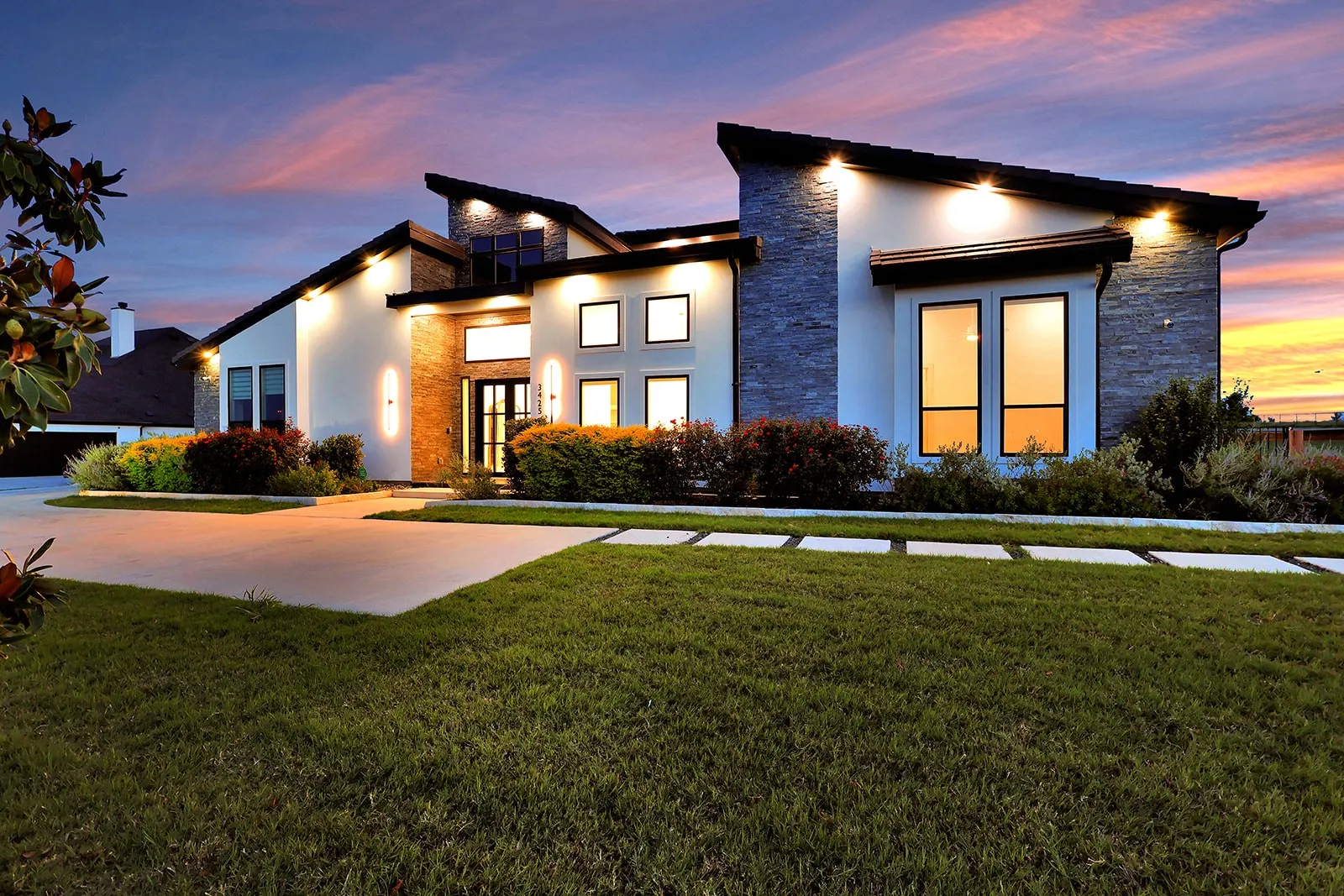Contemporary architectural exterior featuring white stucco and stone accents, a multi-pitch roofline, and integrated exterior lighting