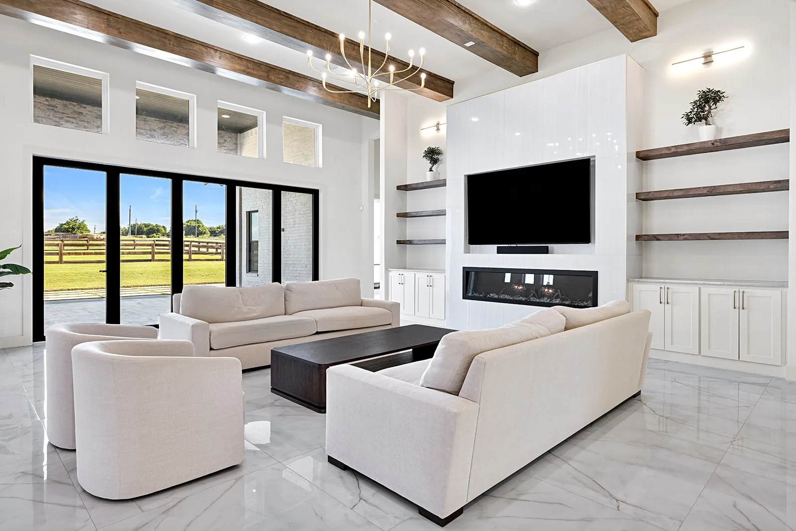 Spacious living area featuring high ceilings with exposed wood beams, a sleek fireplace with integrated media center, and expansive glass doors opening to the exterior