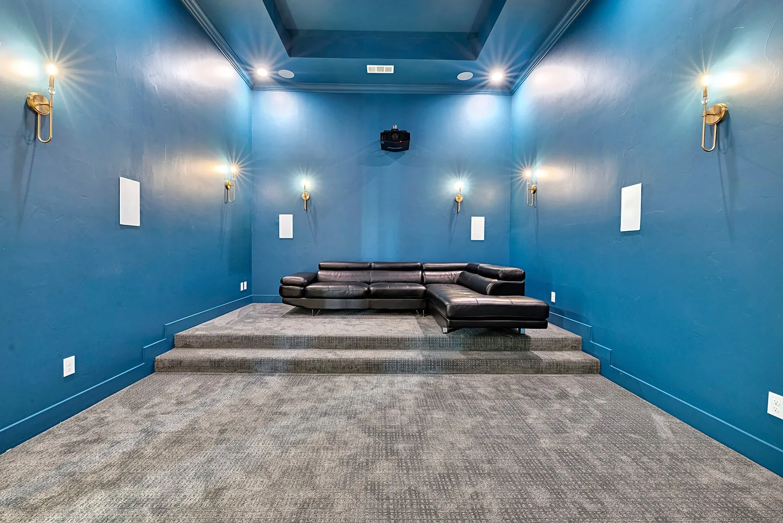 Dedicated media room featuring a tiered platform, wall-mounted speakers, recessed lighting, and sconces