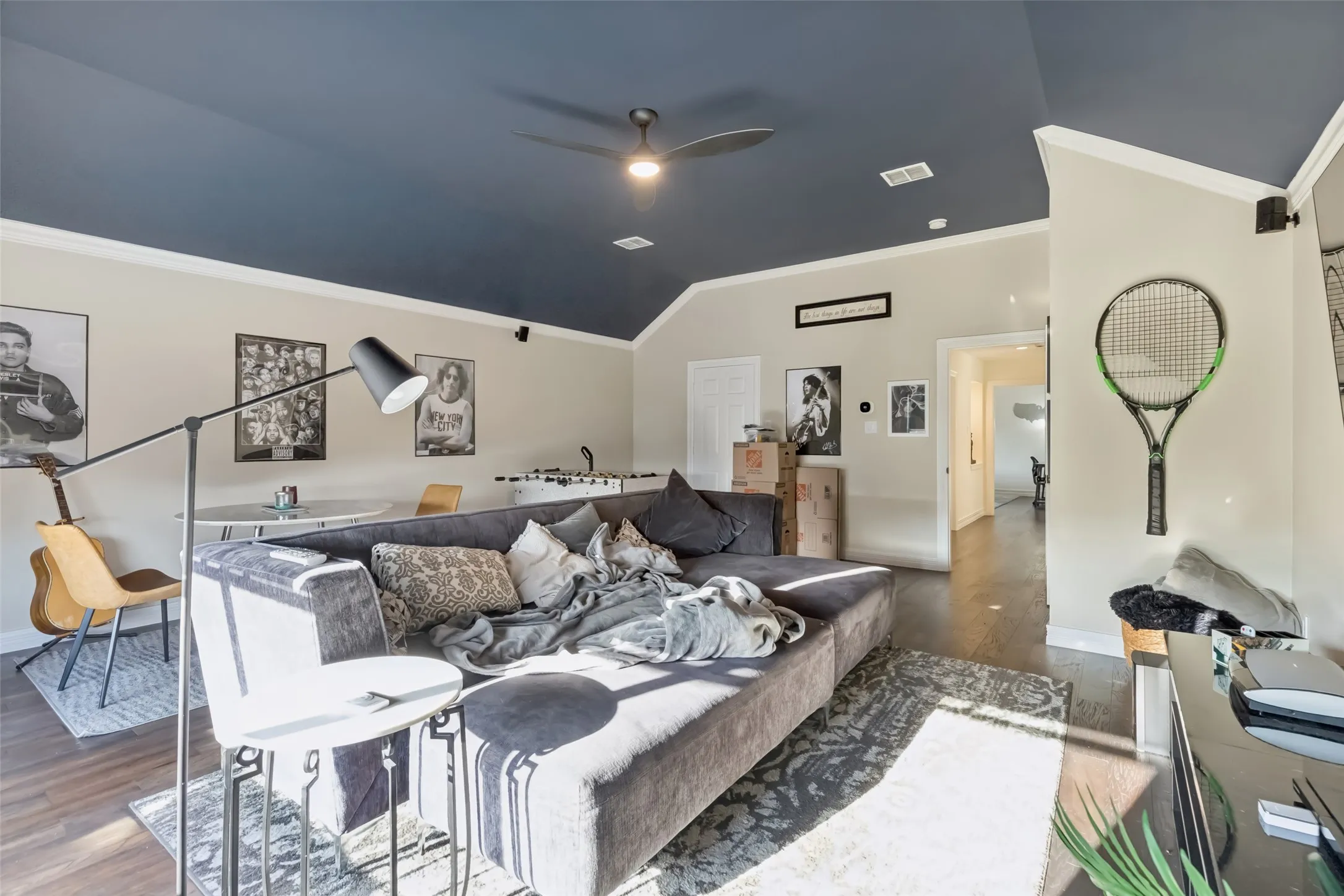 Spacious room featuring wood-finish flooring, a dark ceiling with a ceiling fan, and light-toned walls with white crown molding
