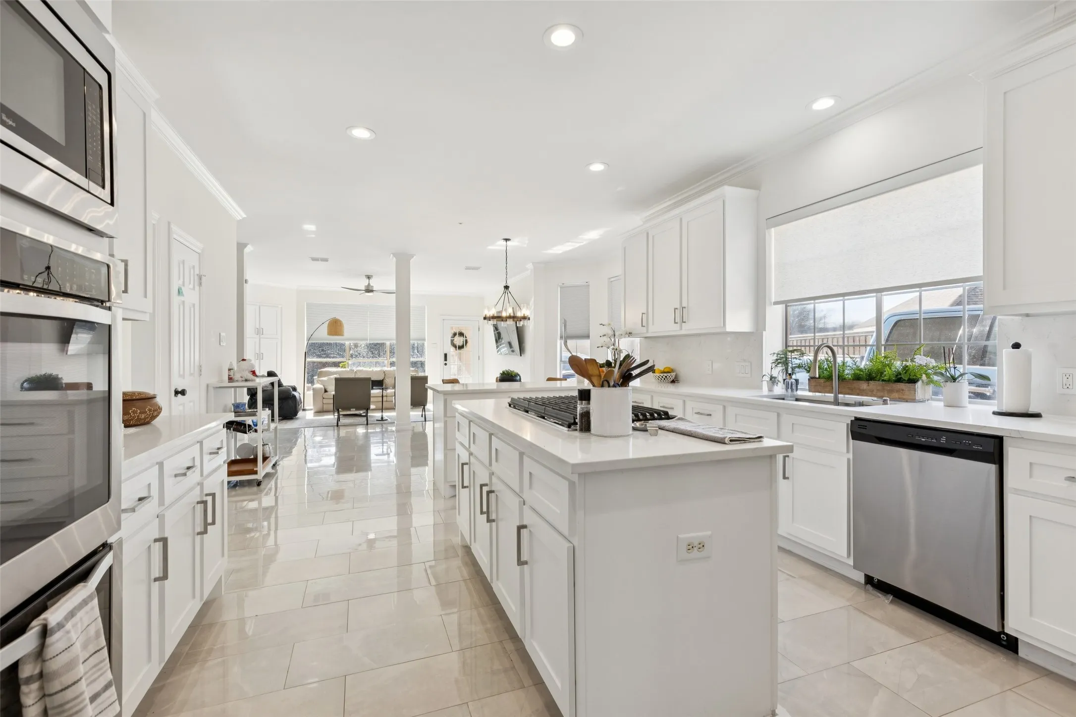 Gourmet kitchen featuring white shaker cabinetry, stainless steel appliances, a center island with cooktop, polished tile flooring, and a large window above the sink