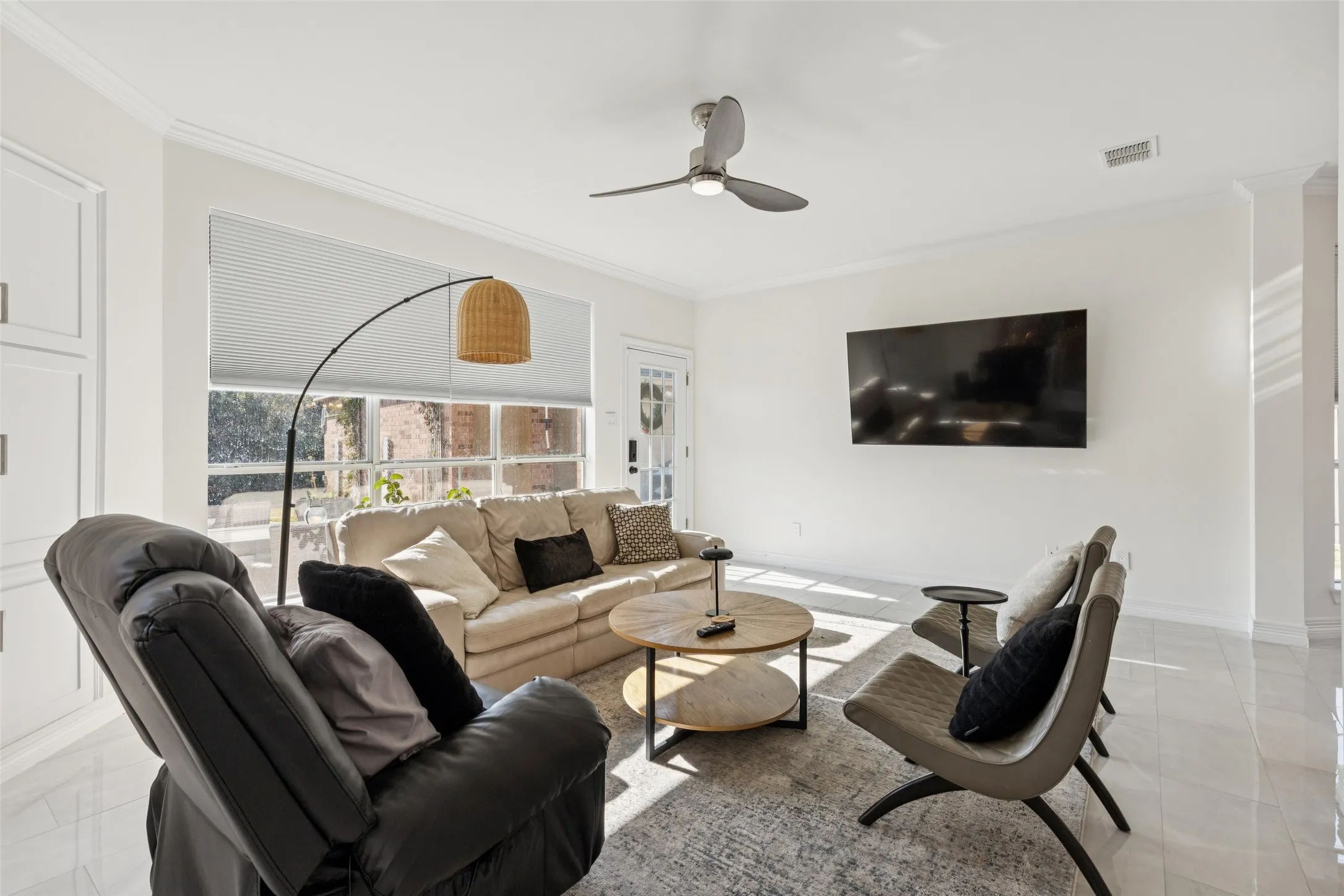 Bright living area featuring polished tile flooring, crown molding, a ceiling fan, and large windows with privacy blinds