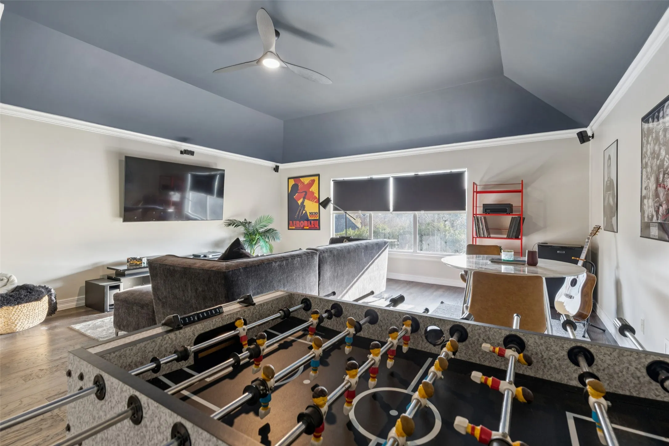 Spacious recreation room featuring wood-finish flooring, a vaulted ceiling with a modern ceiling fan, and multiple windows