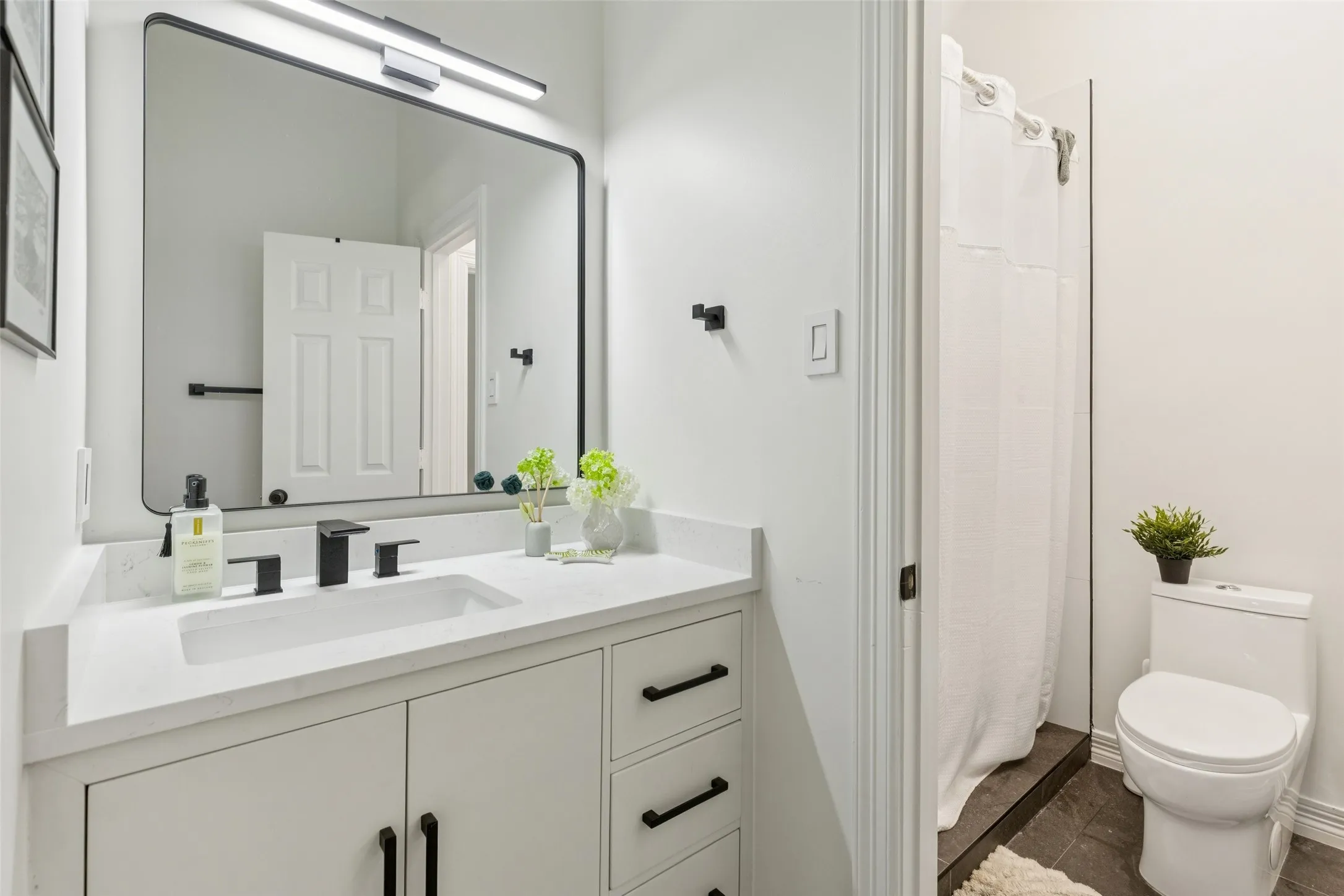 Bathroom featuring a white vanity with integrated sink, a quartz-finish countertop, matte black fixtures, a rectangular mirror with rounded corners, and a tiled shower stall