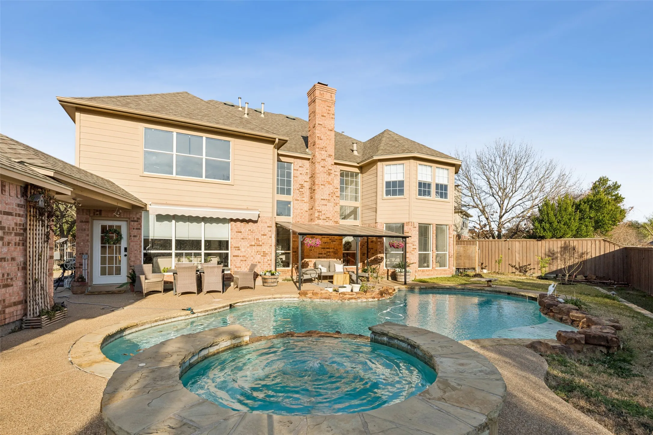 Expansive backyard featuring a freeform swimming pool, integrated spa with natural stone surround, and an adjacent covered patio