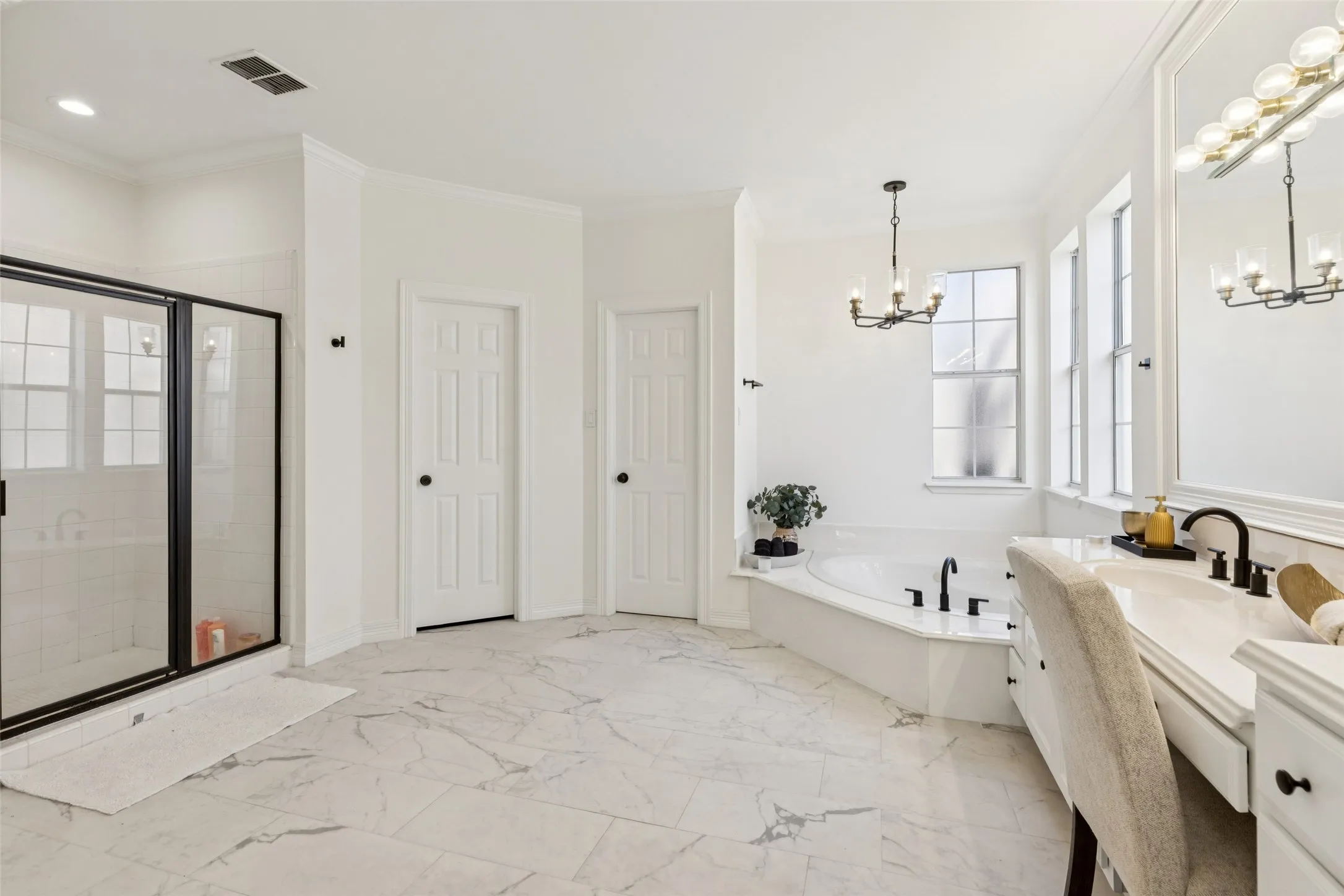 Spacious bathroom featuring marble-look tile flooring, a large corner soaking tub, a walk-in shower with black-framed glass enclosure, and a vanity with a makeup station