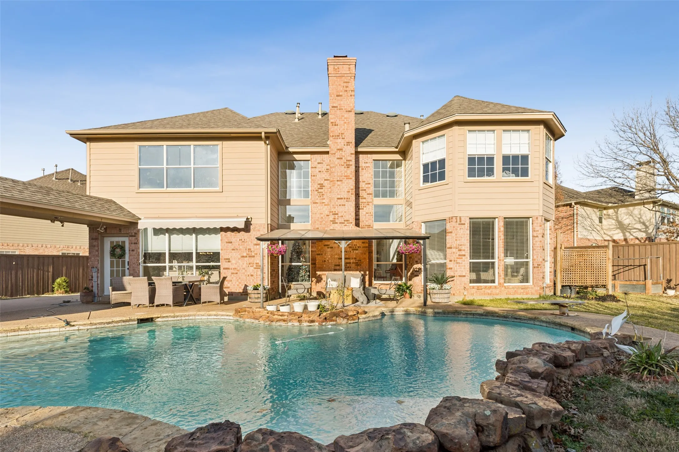Rear exterior featuring a freeform swimming pool with rock coping, a covered patio, and a brick and siding facade